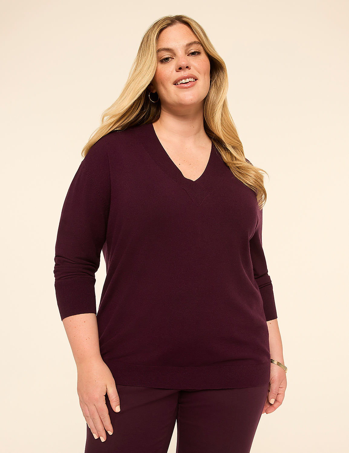 A woman in a plum v-neck sweater and matching pants stands against a plain, light beige background. Product Image 1