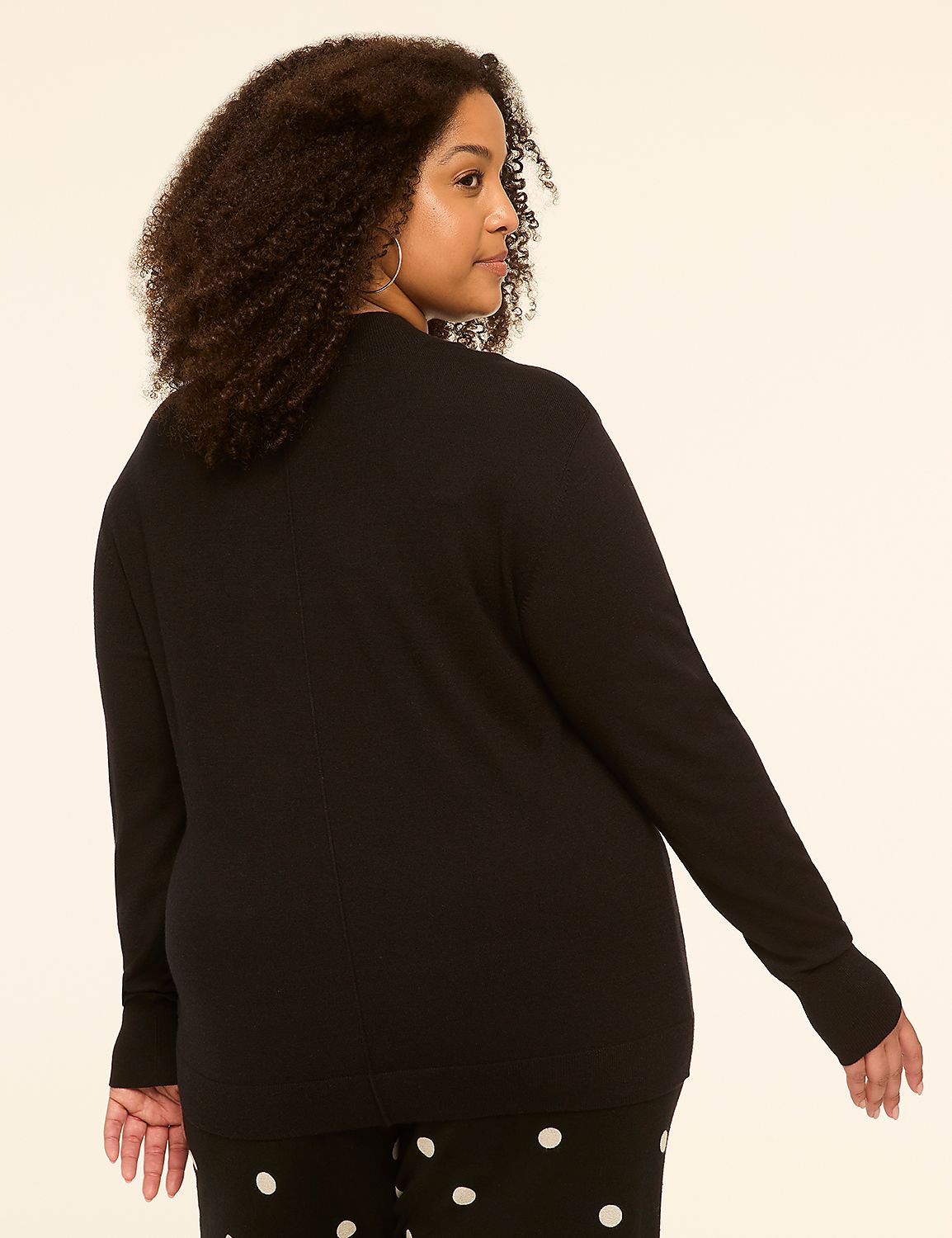 A woman with curly dark hair, wearing a black sweater and polka dot pants, stands against a plain, light-colored background. Product Image 2