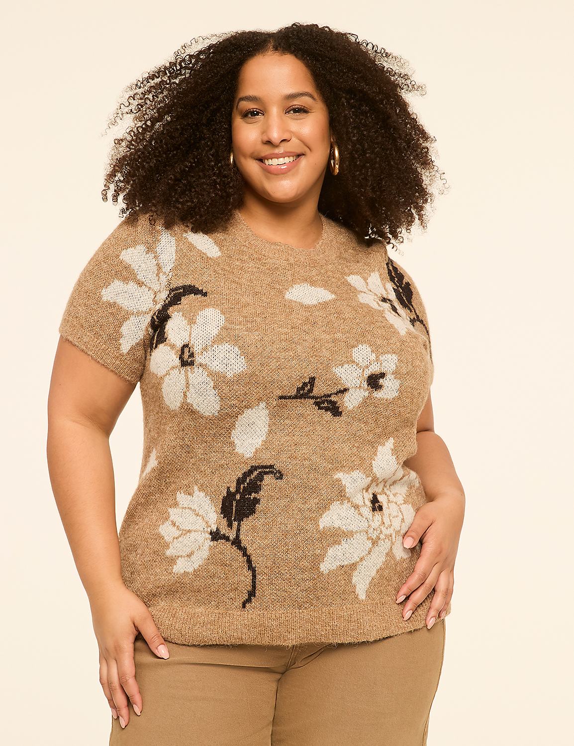 A smiling woman with curly hair wears a tan, floral-patterned sweater and tan pants against a plain, light tan background. Product Image 1