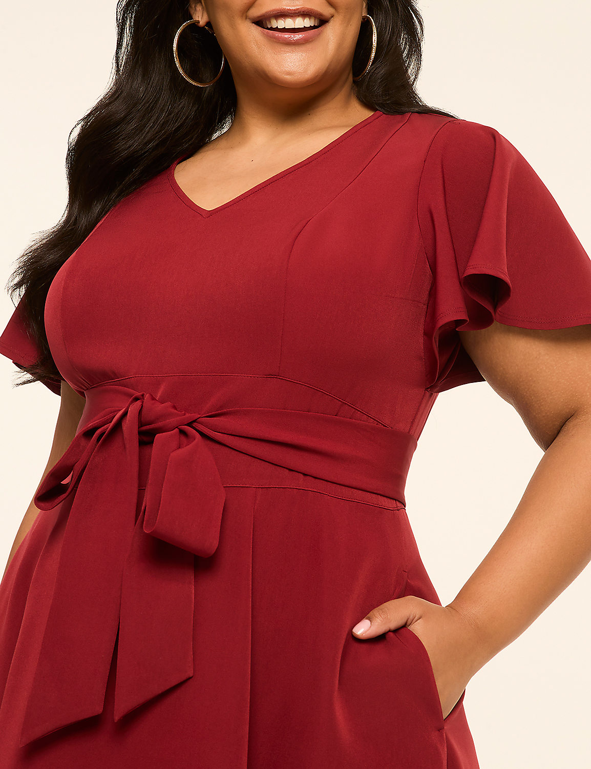 A woman in a red dress with flutter sleeves and a tie waist smiles against a plain cream background. Product Image 3