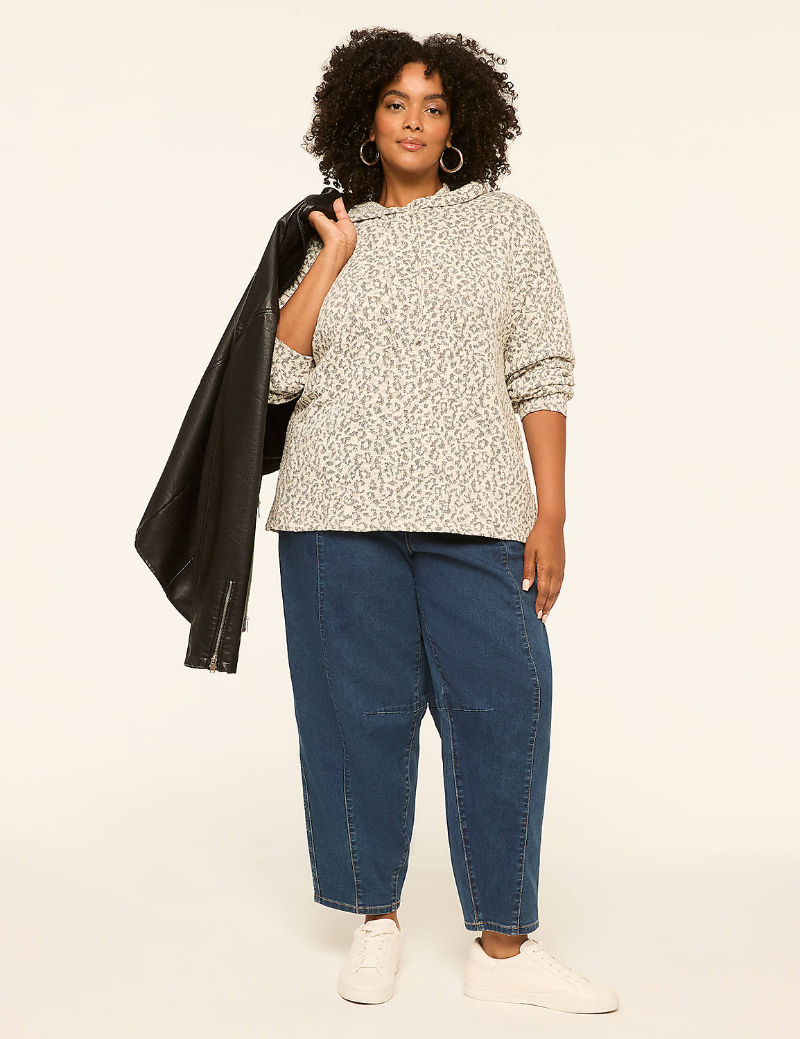 A woman in a leopard-print hoodie and wide-leg jeans stands against a plain, light-colored background, with a black leather jacket draped over her shoulder. Product Image 3