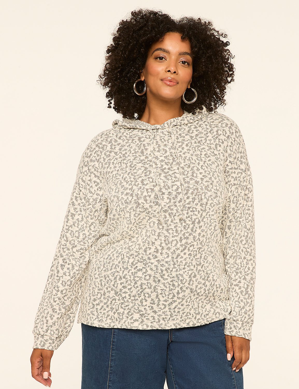 A woman with curly dark hair and hoop earrings stands in the foreground wearing a leopard-print hoodie and blue jeans, against a plain, light-colored background. Product Image 1
