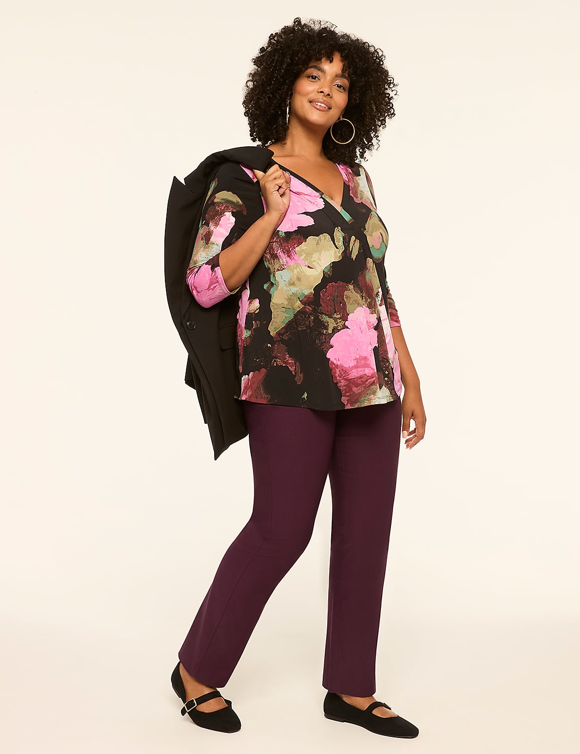 A woman in a floral top and plum pants stands against a plain, light-colored background, with a black jacket draped over her shoulder. Product Image 3