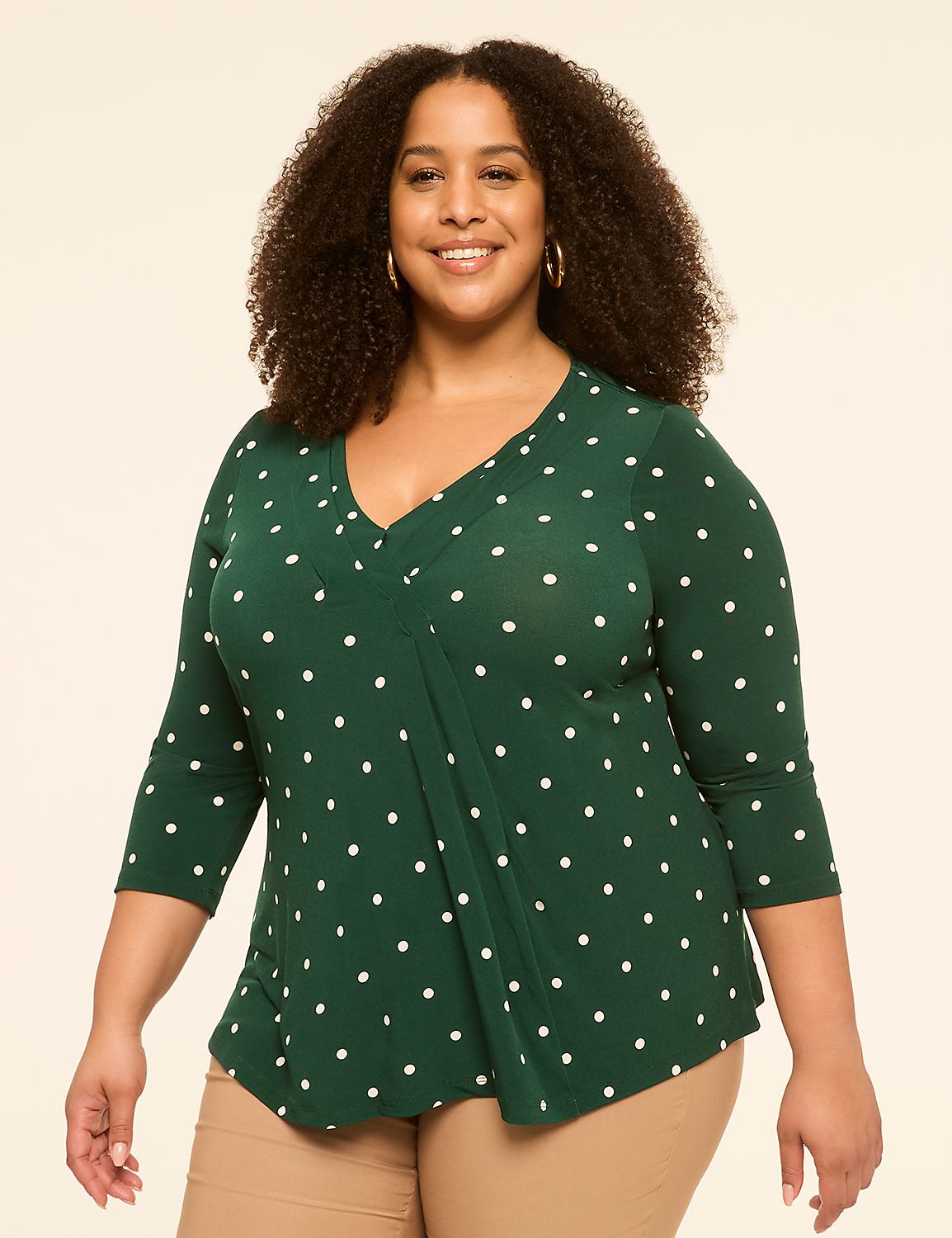 A smiling woman with curly dark hair wears a green polka-dot top and tan pants against a plain, light background. Product Image 1