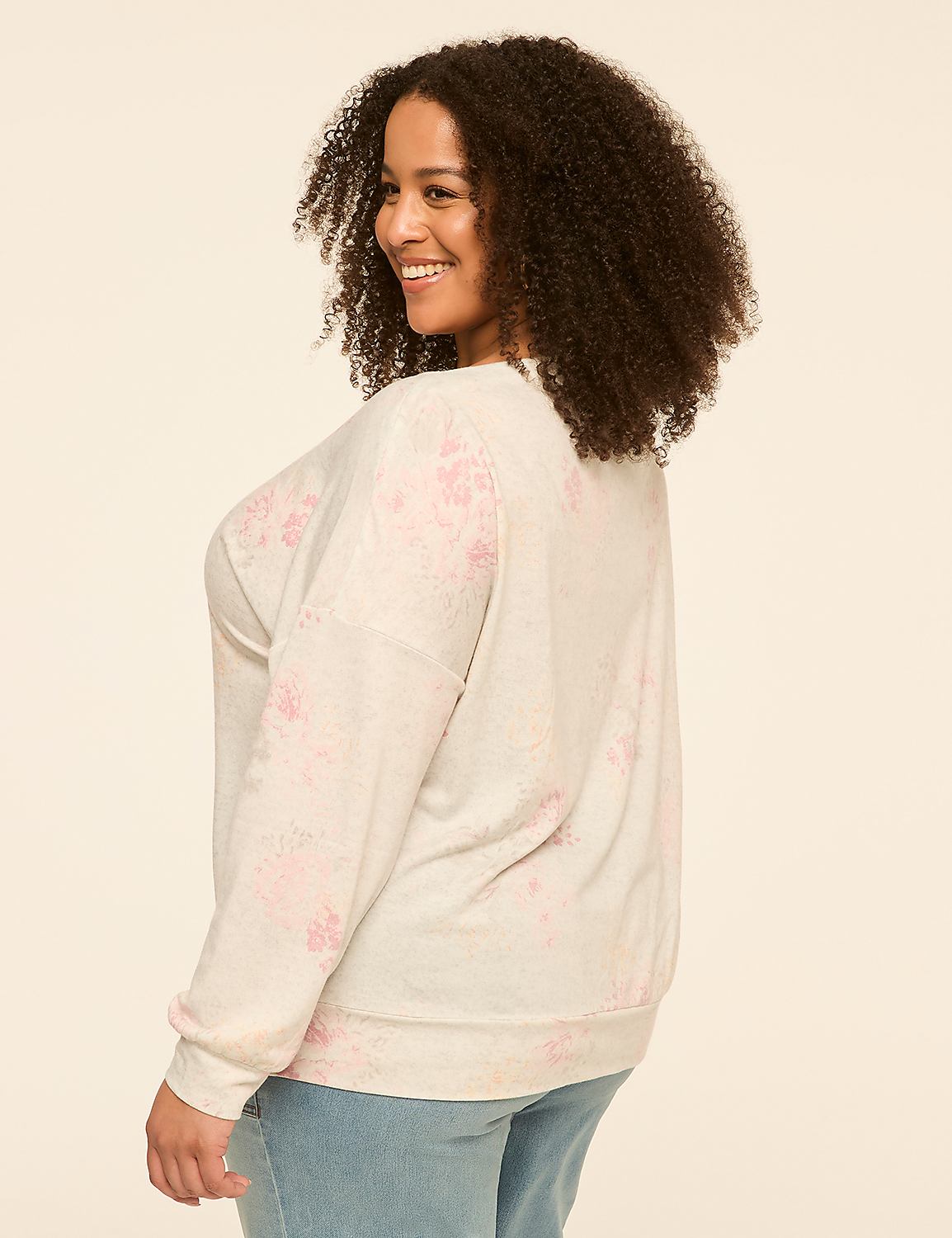 A smiling woman with curly hair in a light-colored, floral-patterned sweater and jeans stands against a plain, light background. Product Image 2