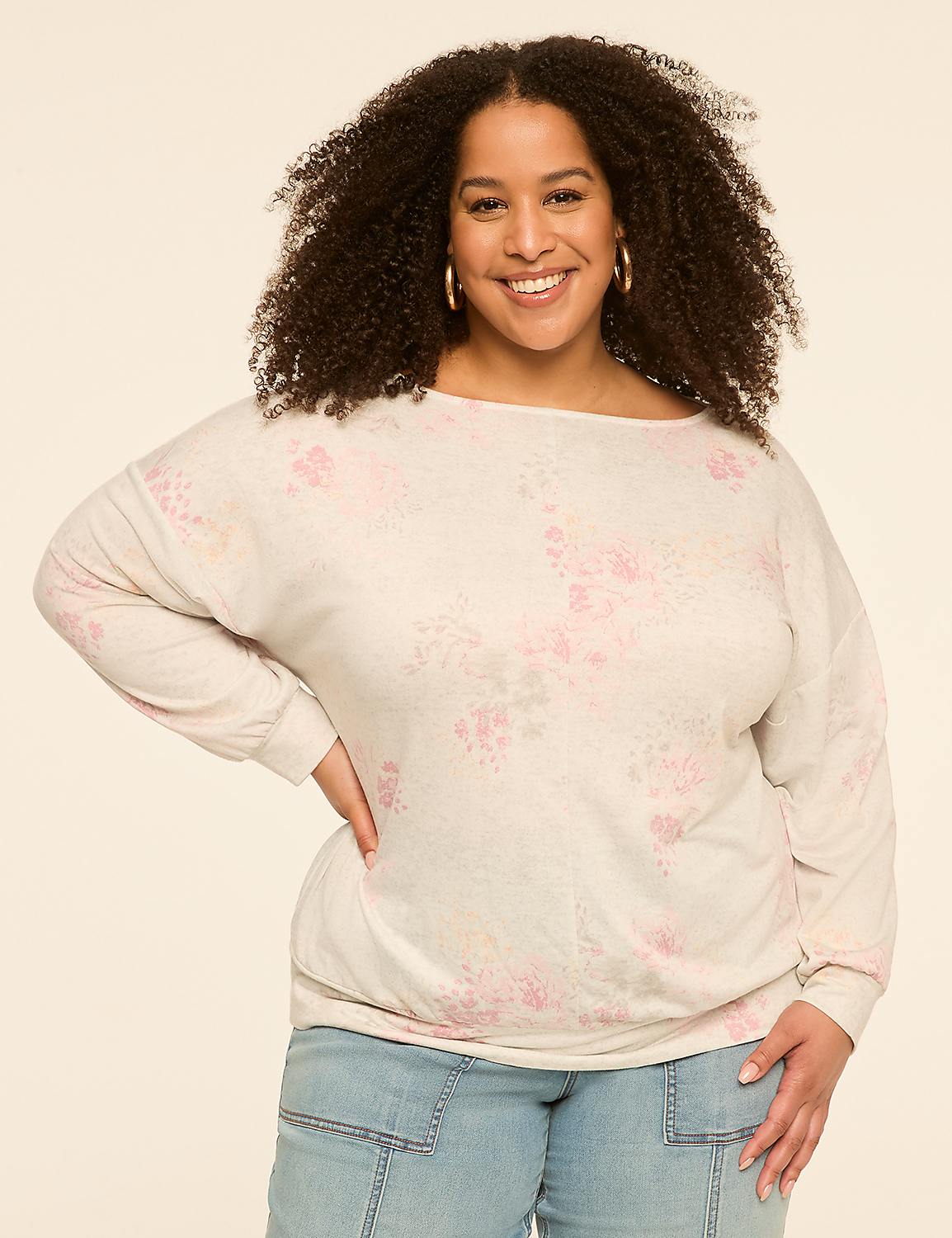 A smiling woman with curly hair poses in a floral sweater and jeans against a plain, light-colored background. Product Image 1