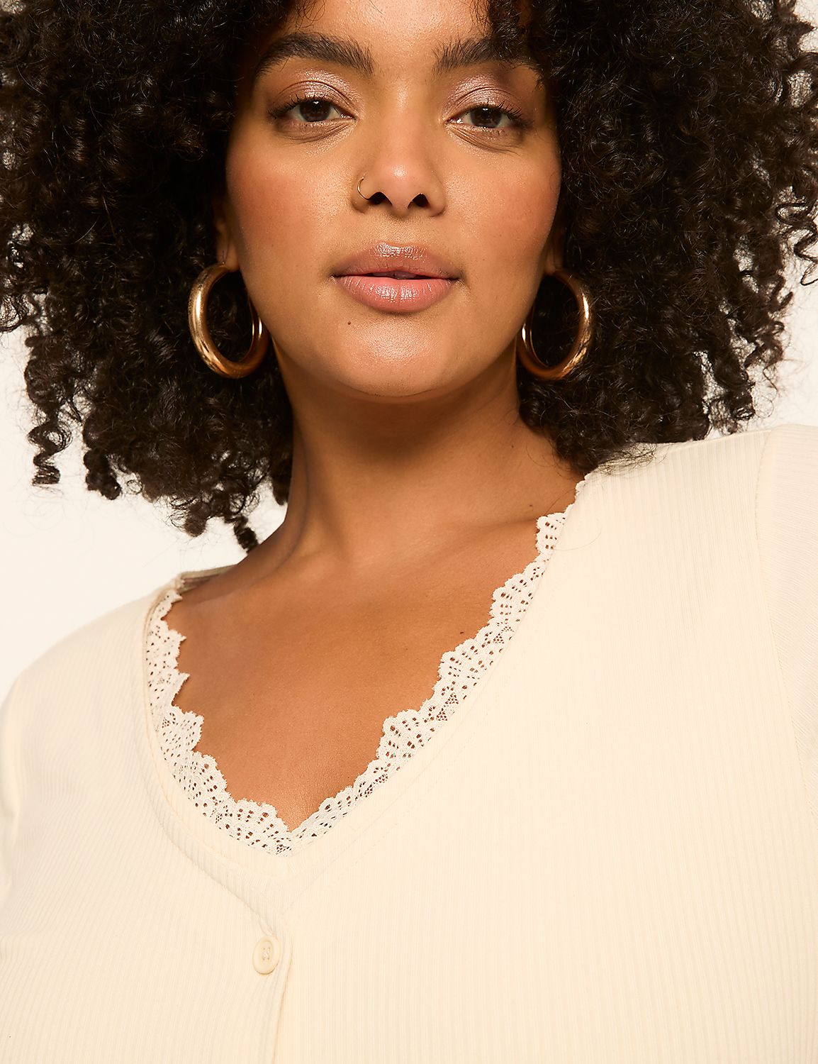 A woman with curly dark hair and large hoop earrings wears a cream-colored, lace-trimmed V-neck top against a plain, light background. Product Image 4