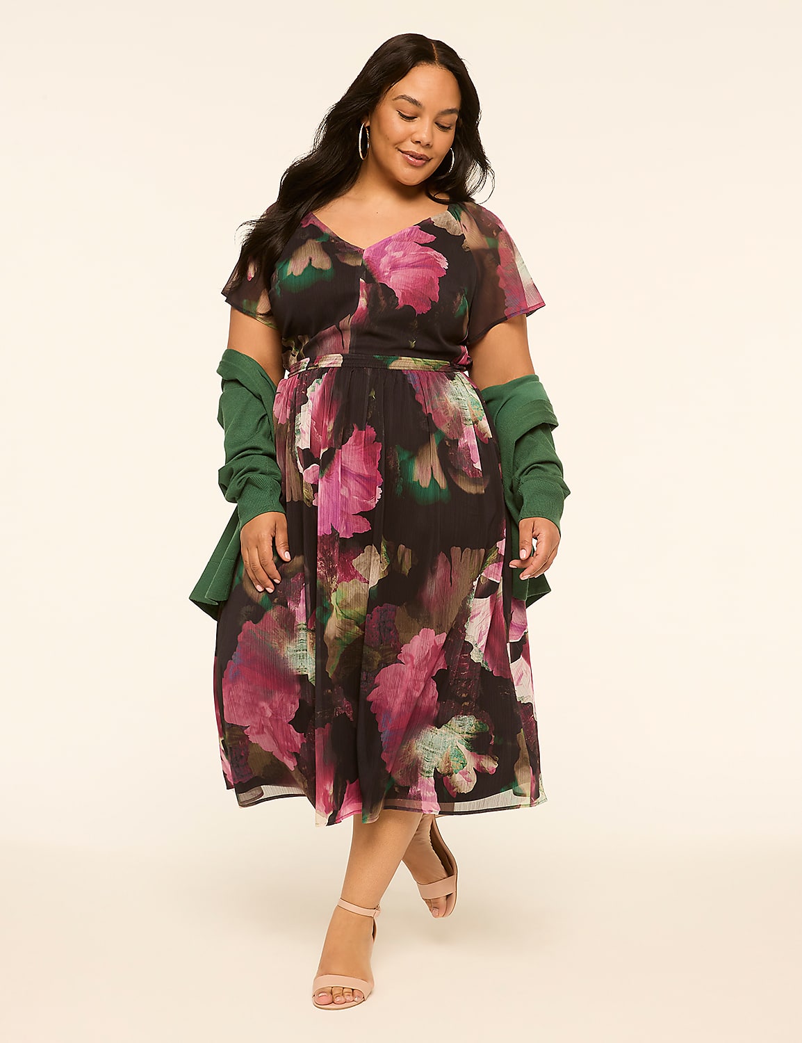 A woman in a floral dress and green jacket stands against a plain, light-colored background. Product Image 1