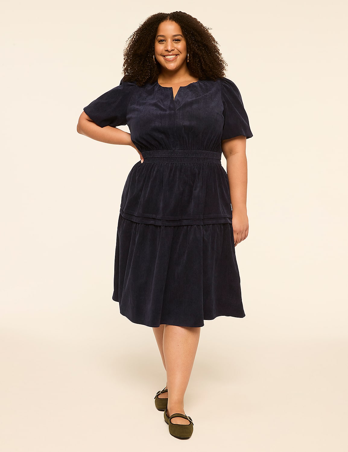 A smiling woman in a navy blue dress stands against a plain, light-colored background. Product Image 1