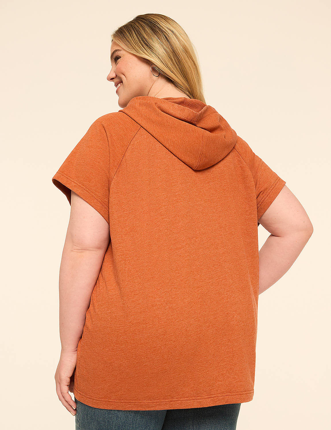 A person in a rust-colored short-sleeved hoodie and blue jeans pulls up the hood against a plain cream background. Product Image 2