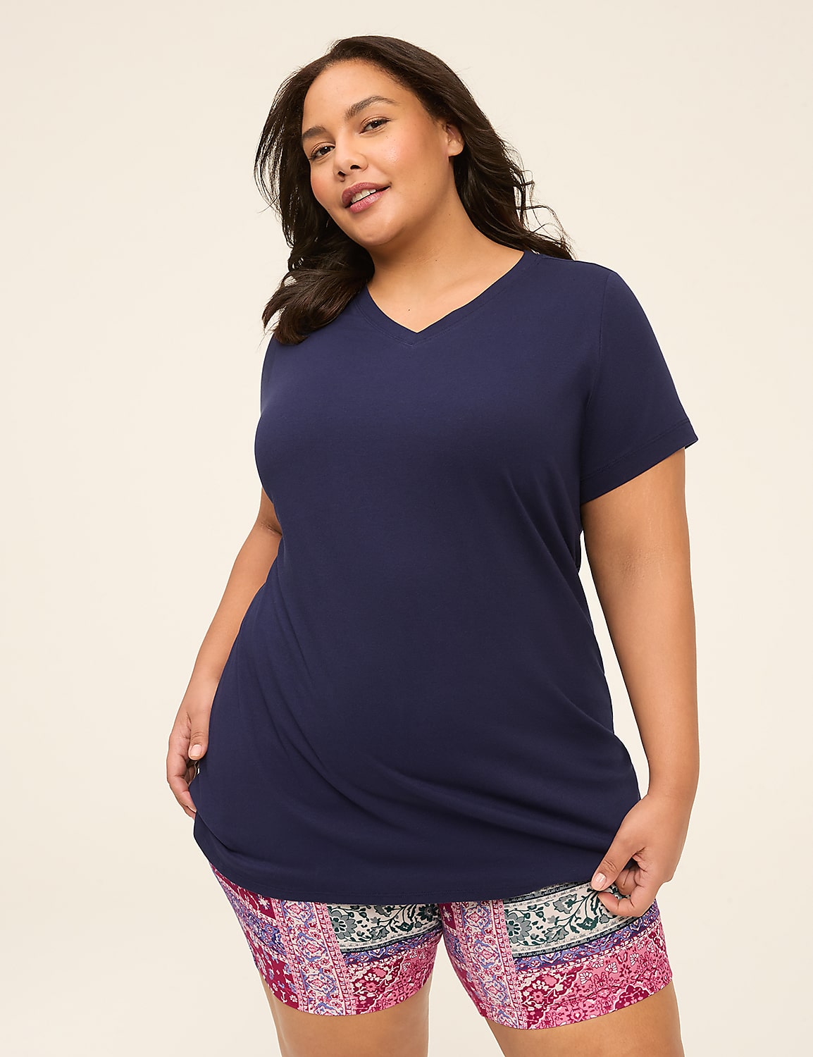 A plus-size woman in a navy v-neck shirt and patterned shorts stands against a plain, light-colored background. Product Image 1