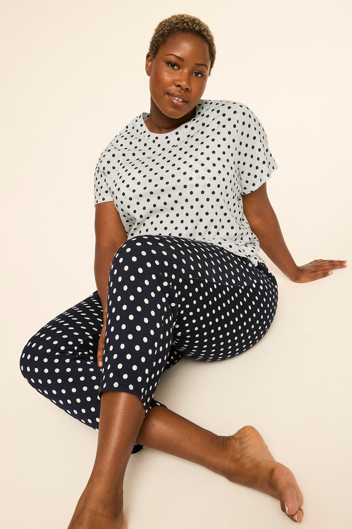 A woman with short hair sits on a plain background, wearing a polka-dot t-shirt and matching pants. Product Image 5