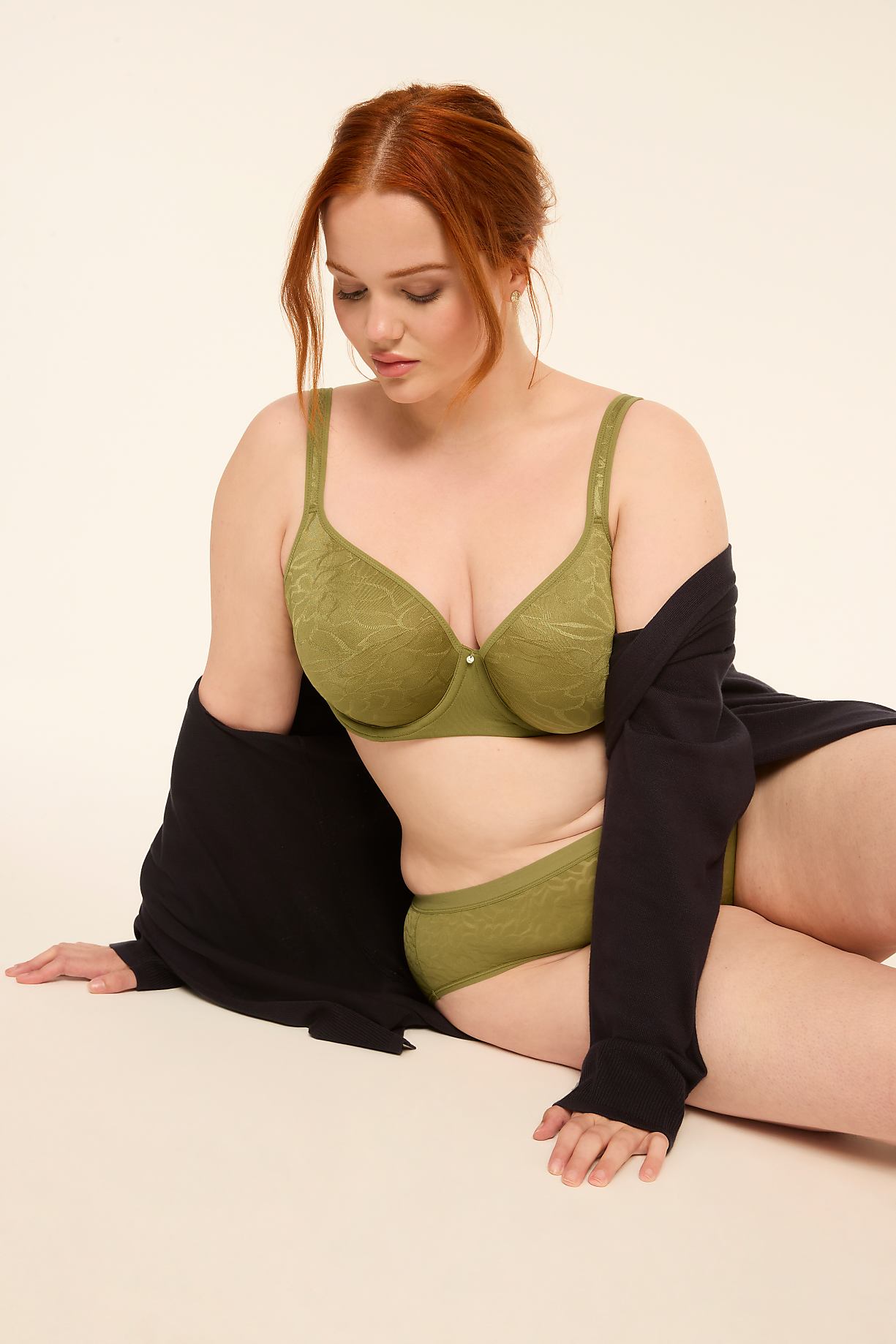 A woman with red hair in a green bra and underwear, draped in a black cardigan, sits against a plain, light-colored background. Product Image 8