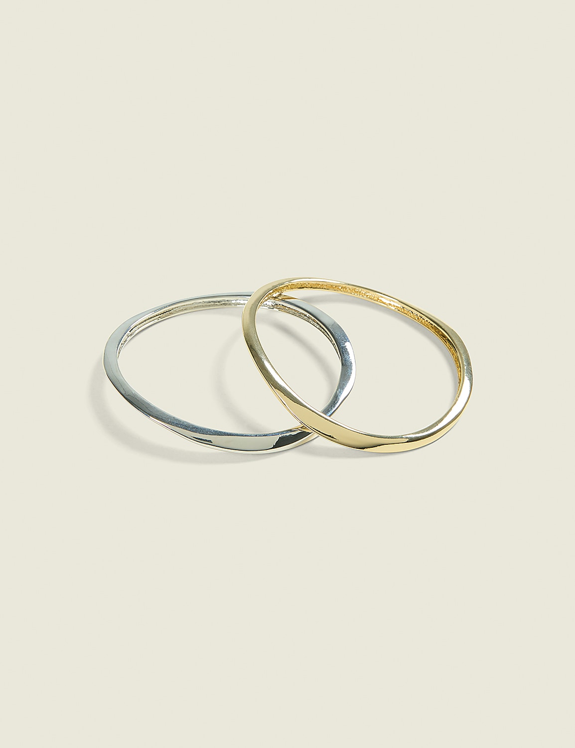 Two intertwined, thin bangles, one silver and one gold, rest on a pale, textured background. Product Image 1