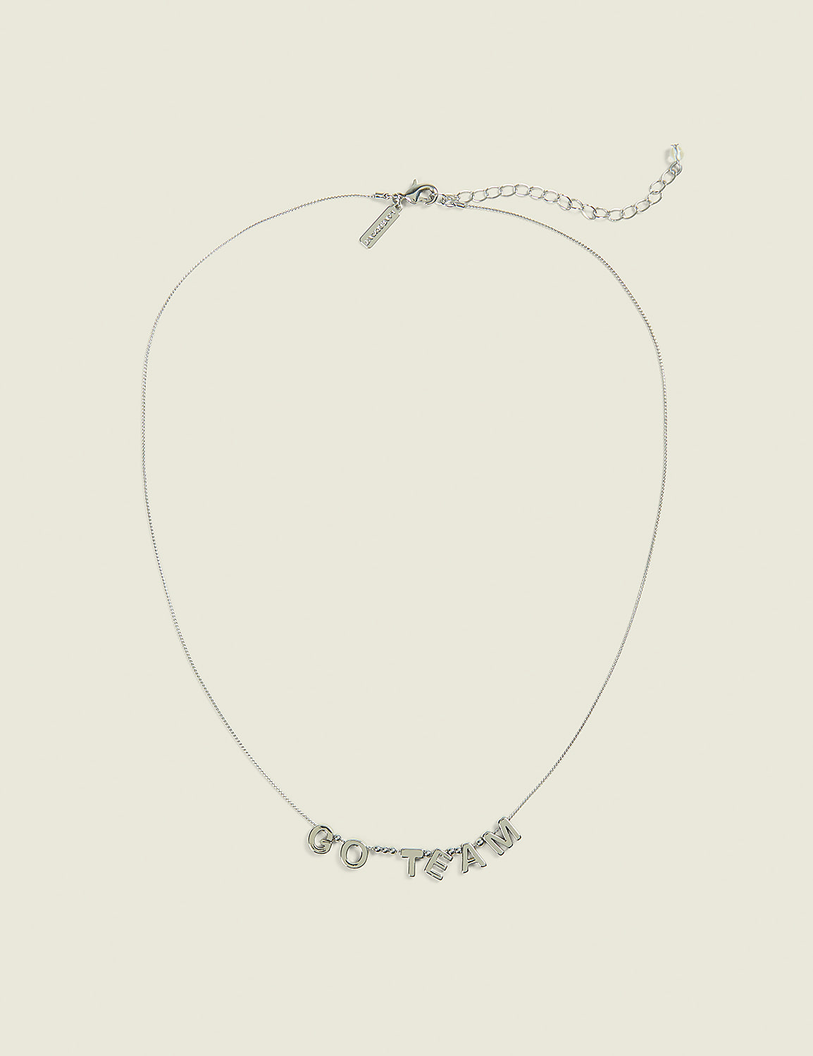 A delicate silver necklace with "GO TEAM" spelled out in block letters rests on a plain, light beige background. Product Image 1