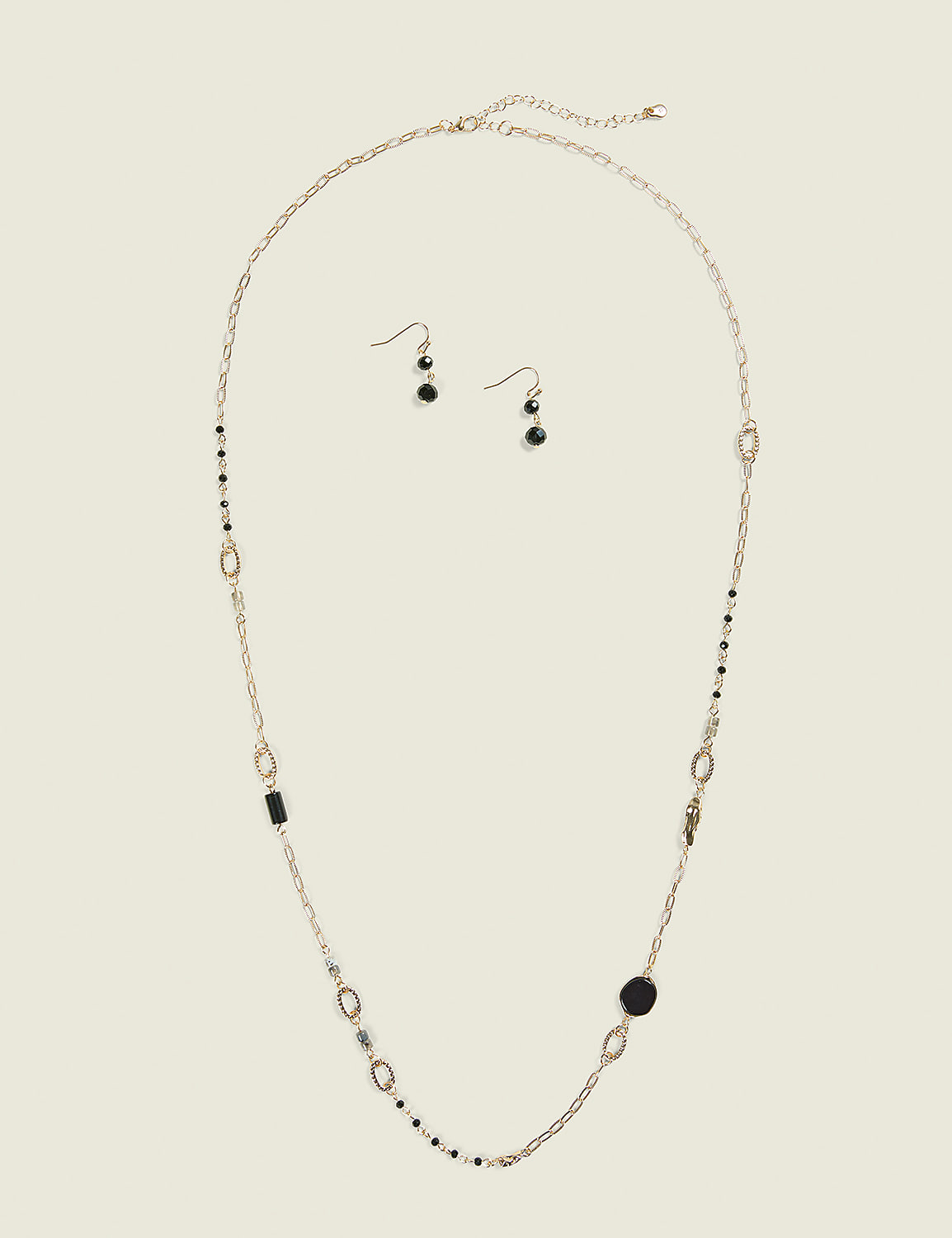 A long gold necklace with black and silver beads and charms, along with a pair of matching earrings, are laid out on a plain, light beige background. Product Image 1
