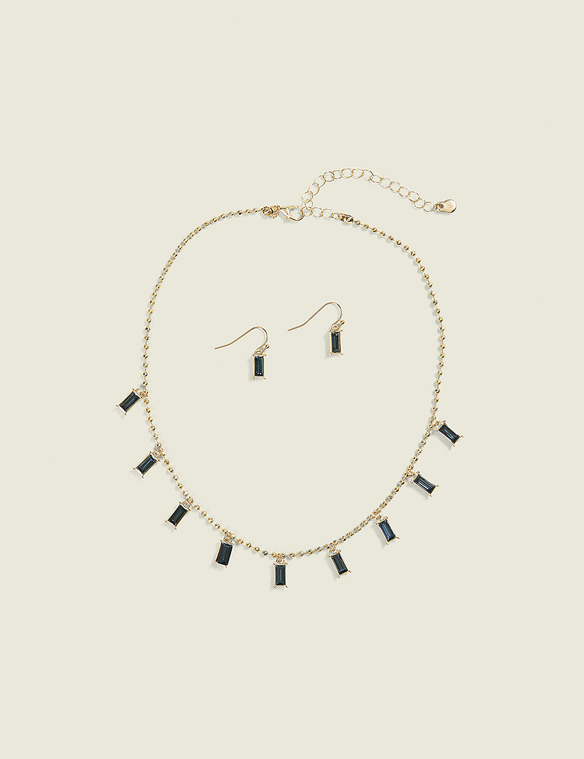 A gold necklace with dangling rectangular blue gems and matching earrings rests on a plain, light beige background. Product Image 1