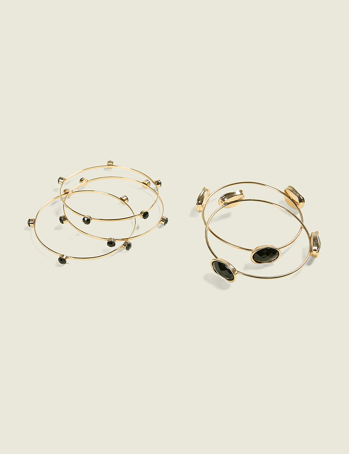 Two sets of thin gold bangles, one with small black stones and the other with larger faceted black stones, rest on a plain, light-colored background. Product Image 1