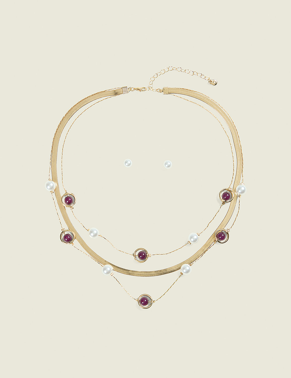 A layered gold necklace with pearls and purple beads rests on a plain, light-colored background, with a pair of pearl stud earrings positioned above it. Product Image 1