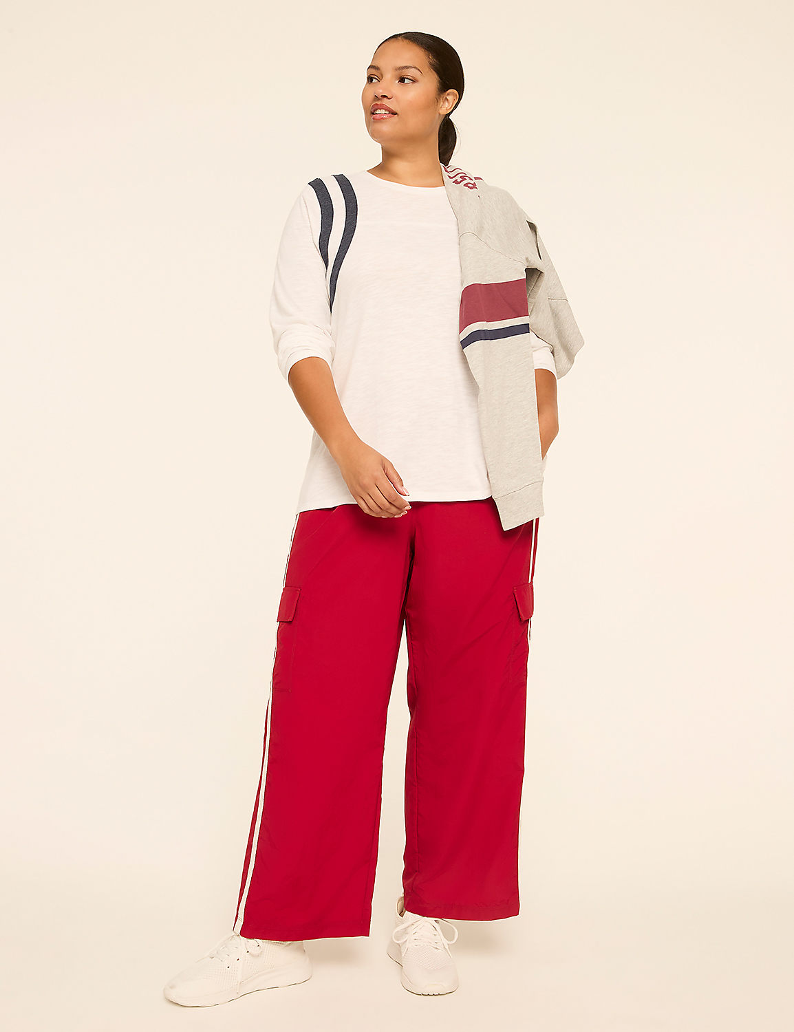 A woman in a white shirt and red pants stands against a plain, light-colored background, with a gray and red striped jacket draped over her shoulders. Product Image 3