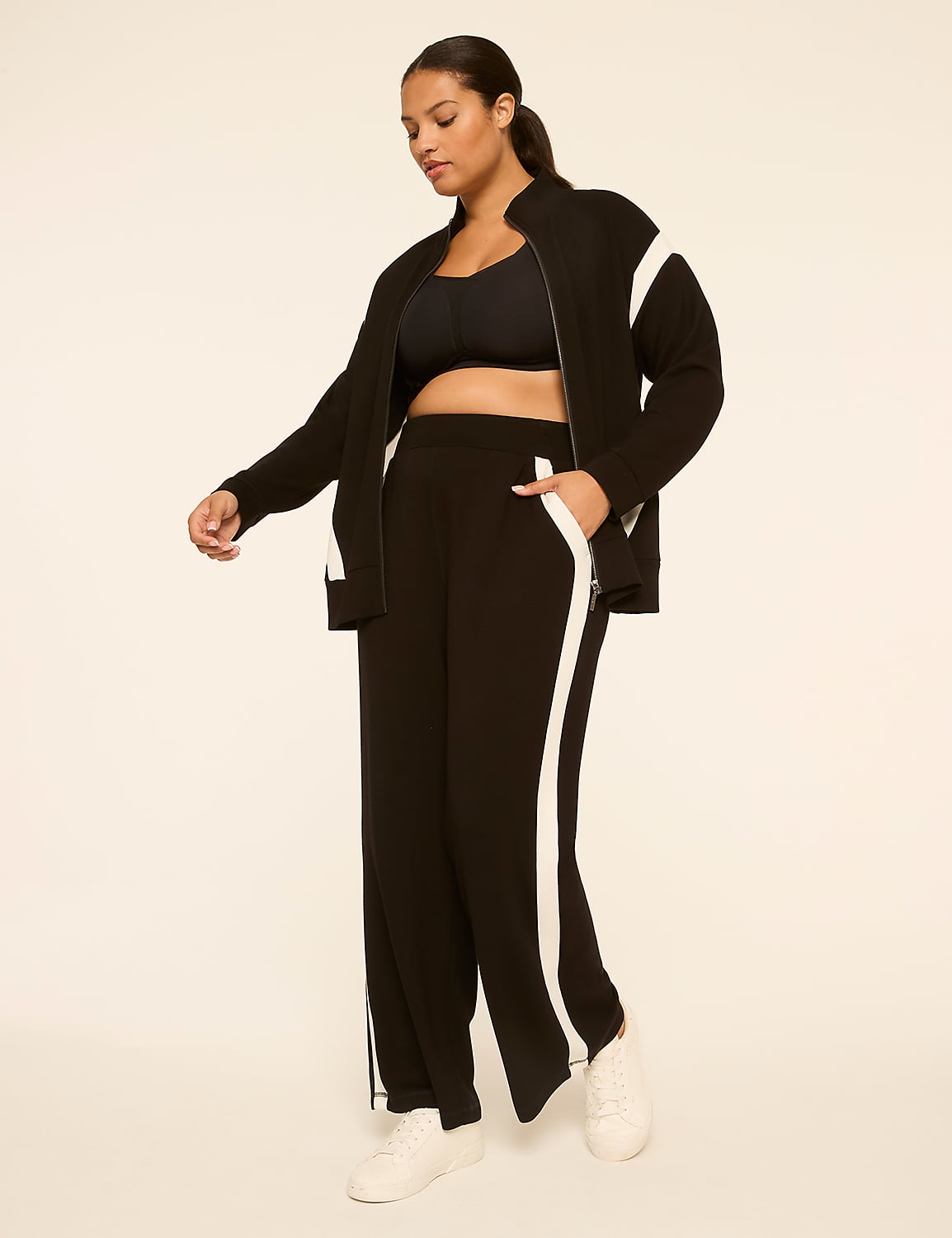 A woman in a black tracksuit with white stripes stands against a plain, light-colored background. Product Image 3
