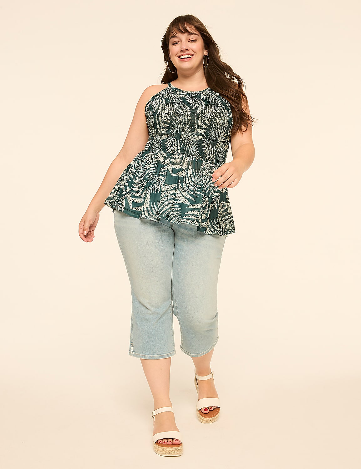 A smiling woman in a patterned peplum top and light wash capri jeans walks forward against a plain, light background. Product Image 3