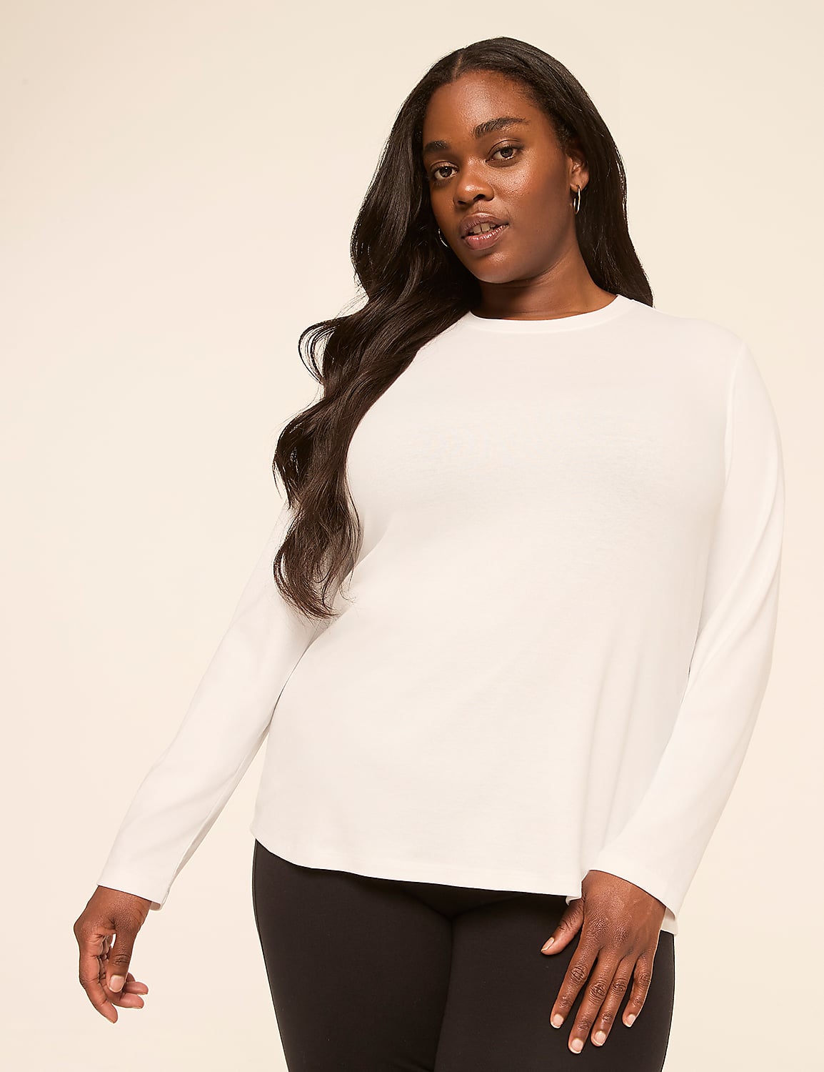 A woman with long, dark hair wears a white long-sleeved shirt and black leggings against a plain, light-colored background. Product Image 1