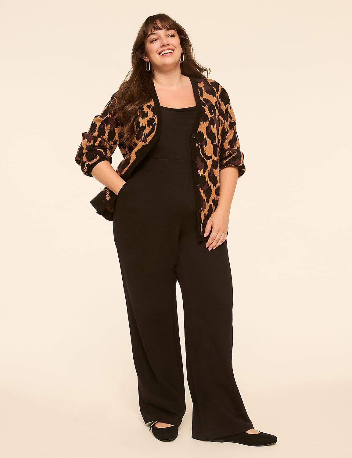 A smiling woman in a black jumpsuit and leopard print cardigan stands against a plain, light-colored background. Product Image 3