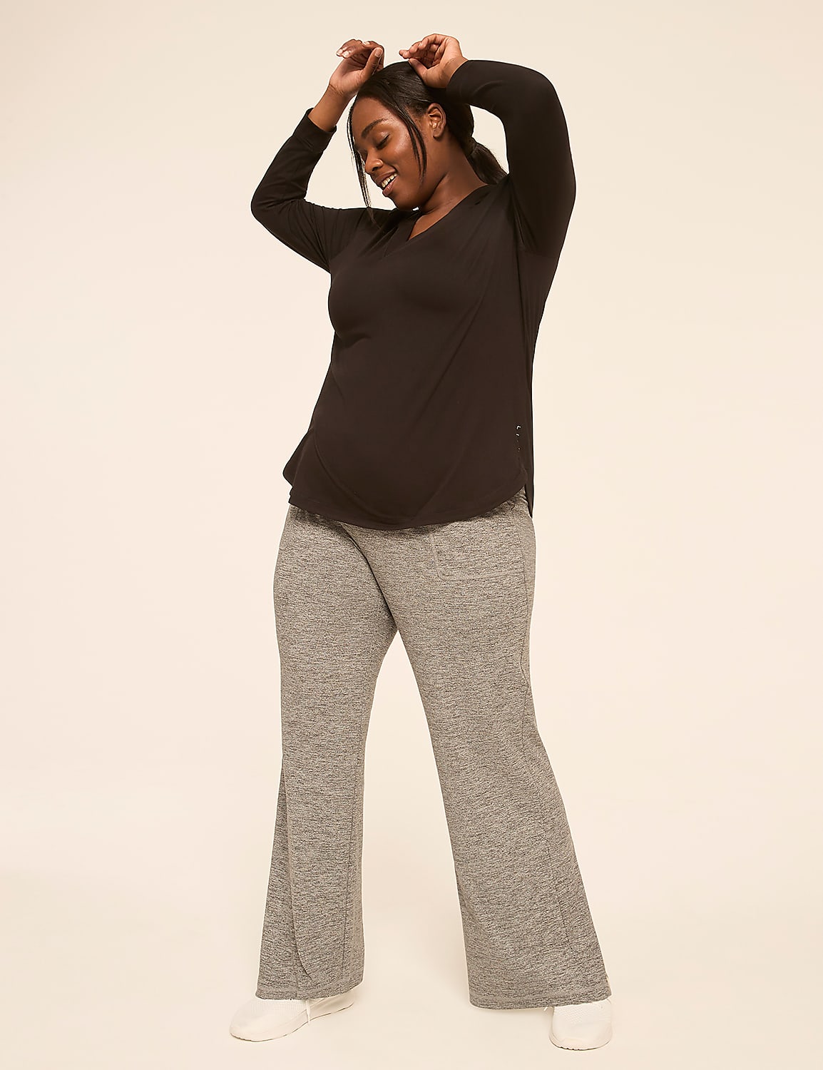 A woman in a black top and grey sweatpants poses with her arms raised against a plain, light-colored background. Product Image 3