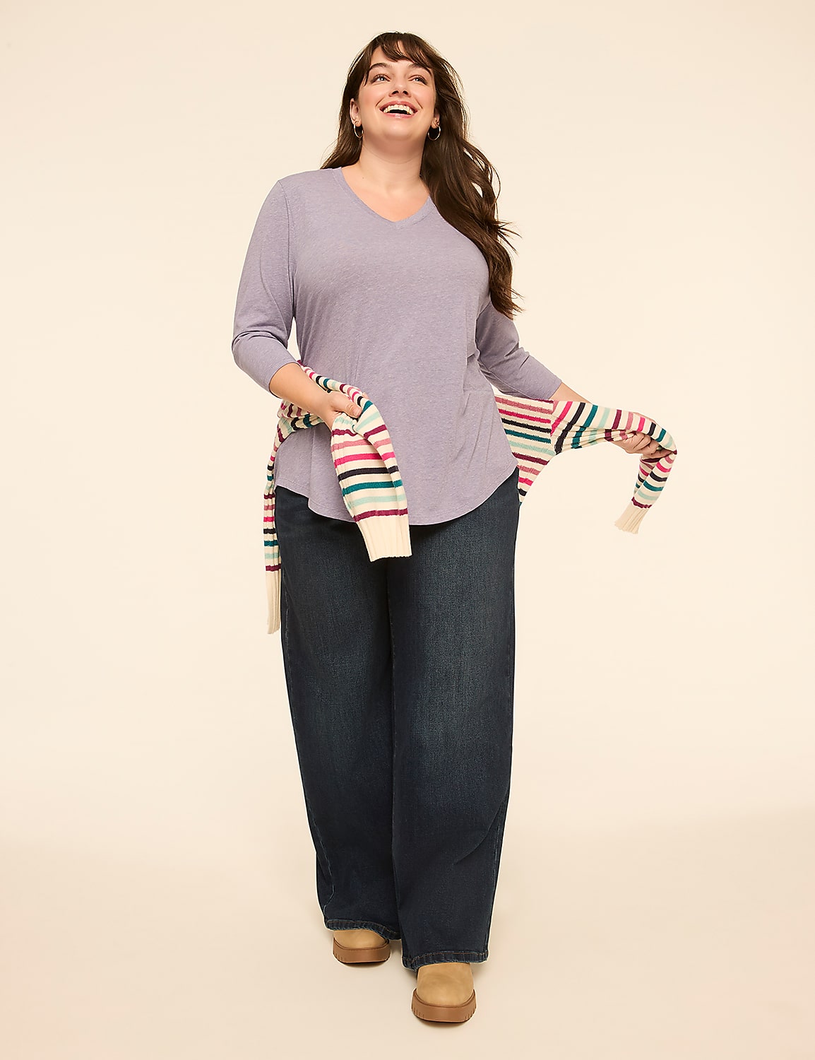 A smiling woman in a light purple striped shirt and dark wide-leg jeans stands against a plain, light-colored background, with a striped sweater draped over her shoulders. Product Image 3