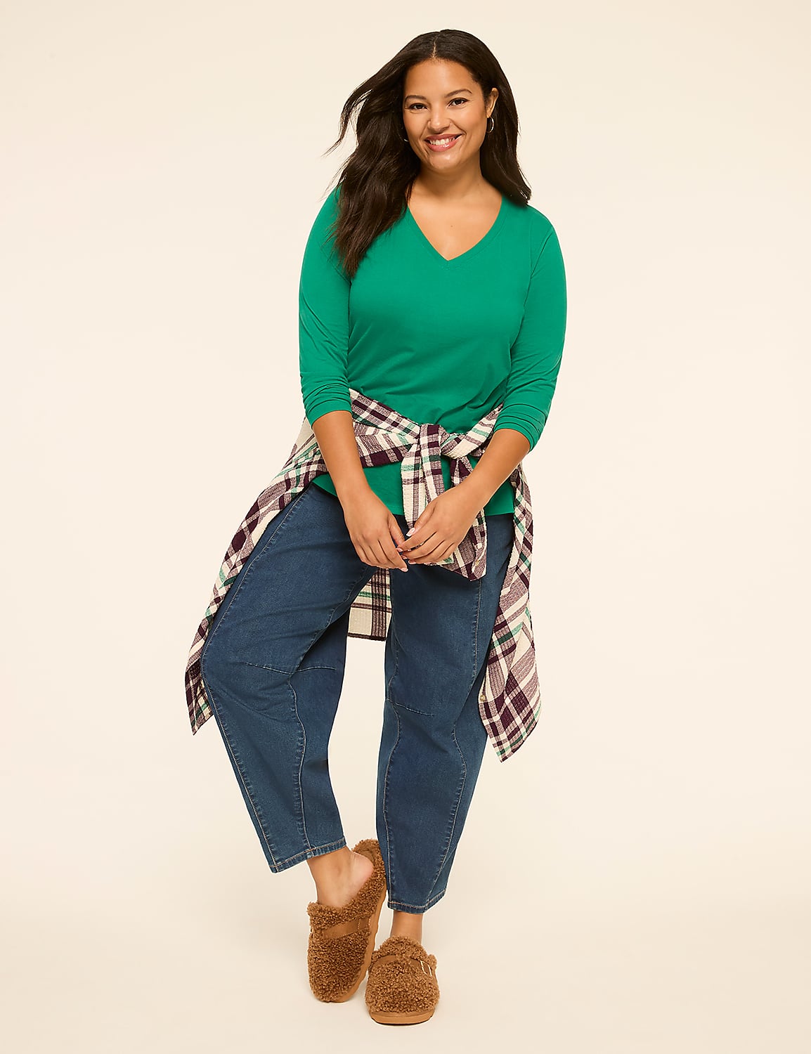 A smiling woman in a green shirt, blue jeans, and fuzzy slippers stands against a plain, light-colored background with a plaid shirt tied around her waist. Product Image 3