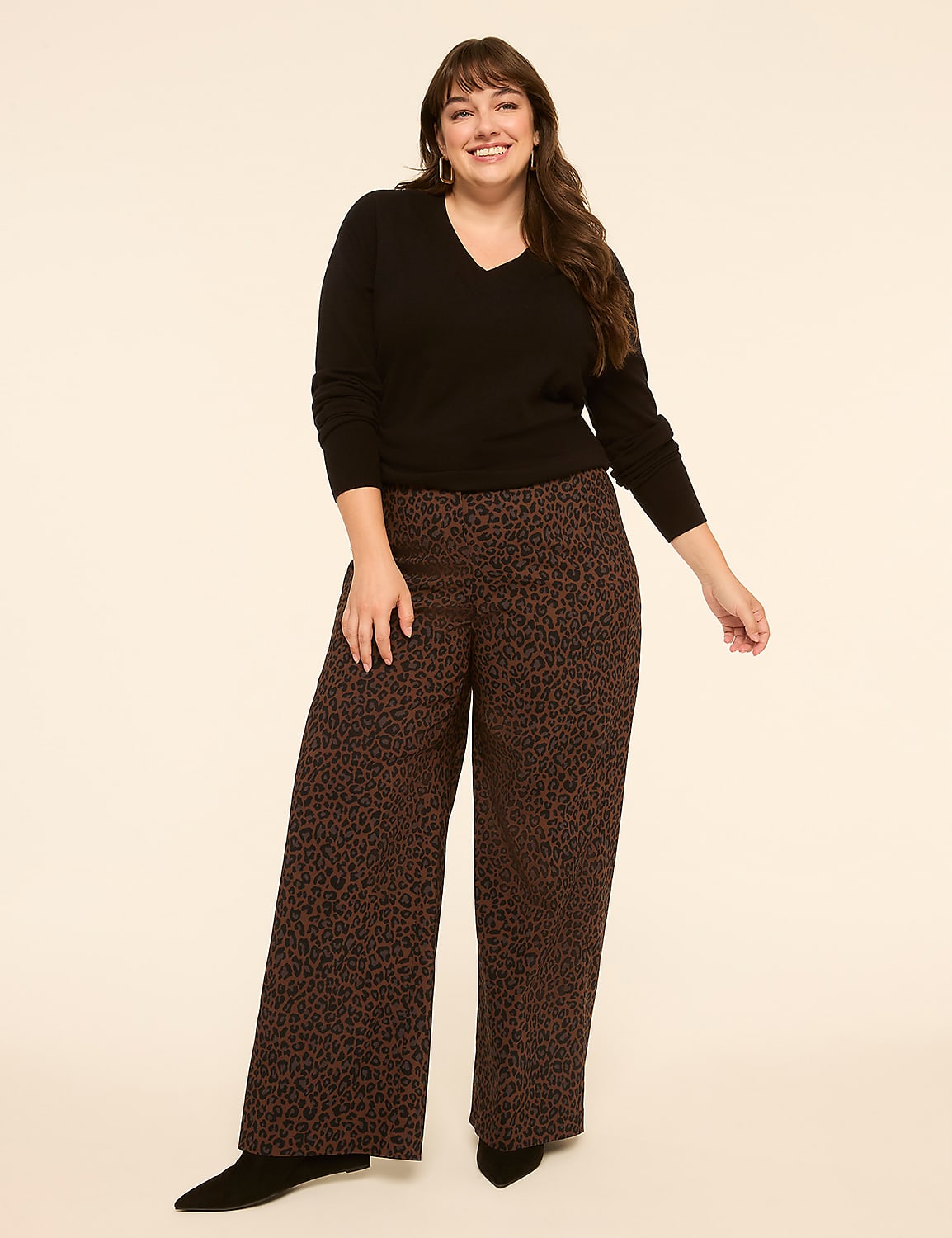 A smiling woman in a black v-neck sweater and leopard print wide-leg pants stands against a plain, light-colored background. Product Image 3