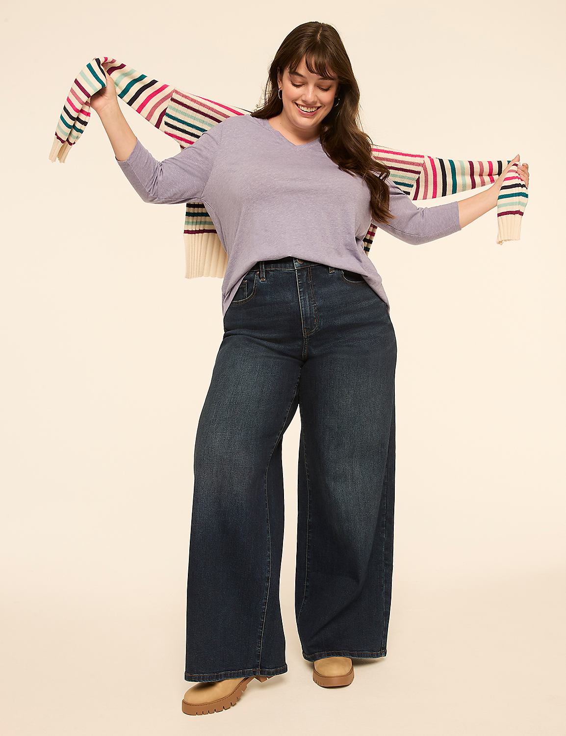 A smiling woman in wide-leg jeans and a lavender sweater poses with a striped scarf draped over her shoulders against a plain, light-colored background. Product Image 3