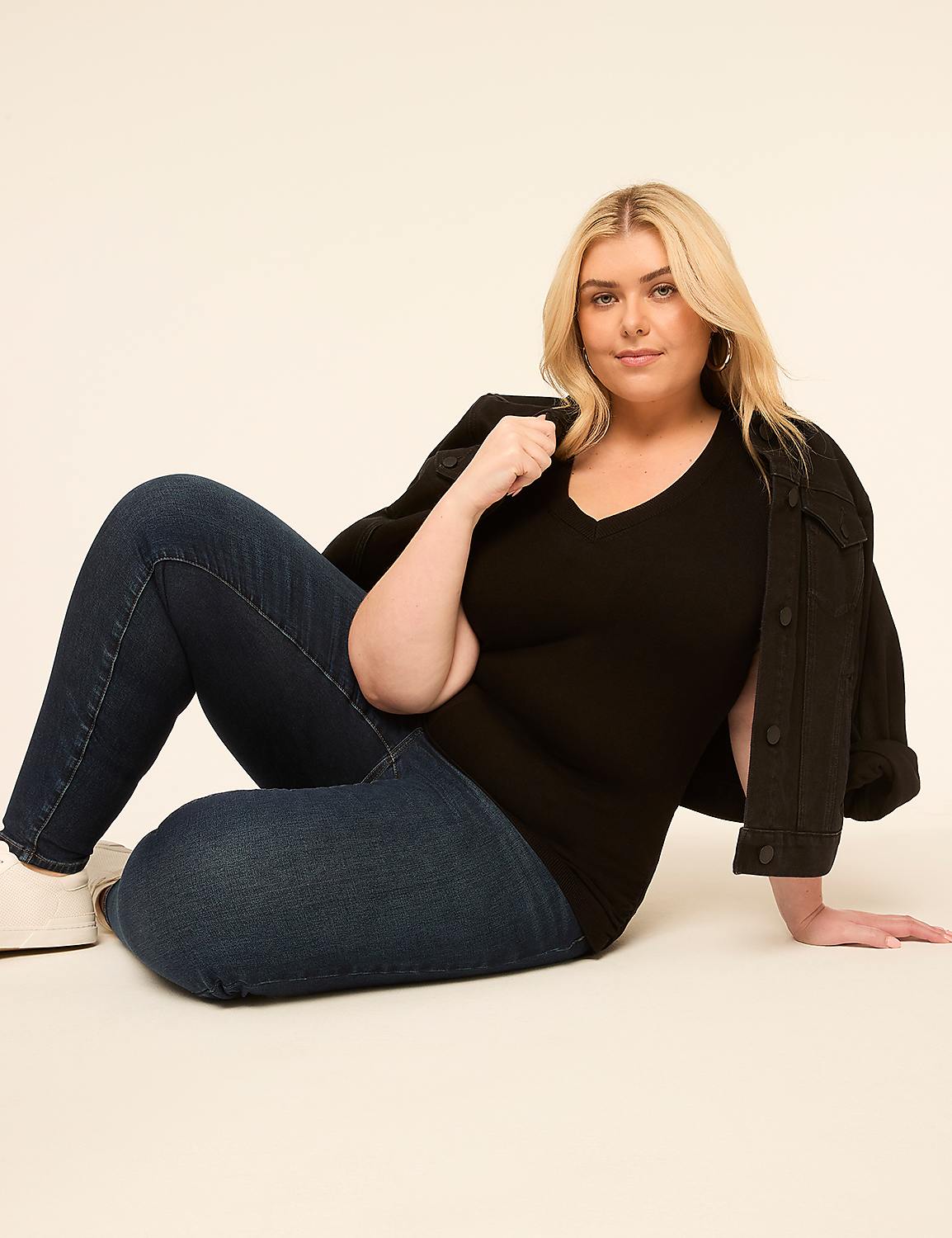 A woman in a black v-neck shirt and jeans sits on a light-colored floor with a plain background. Product Image 3