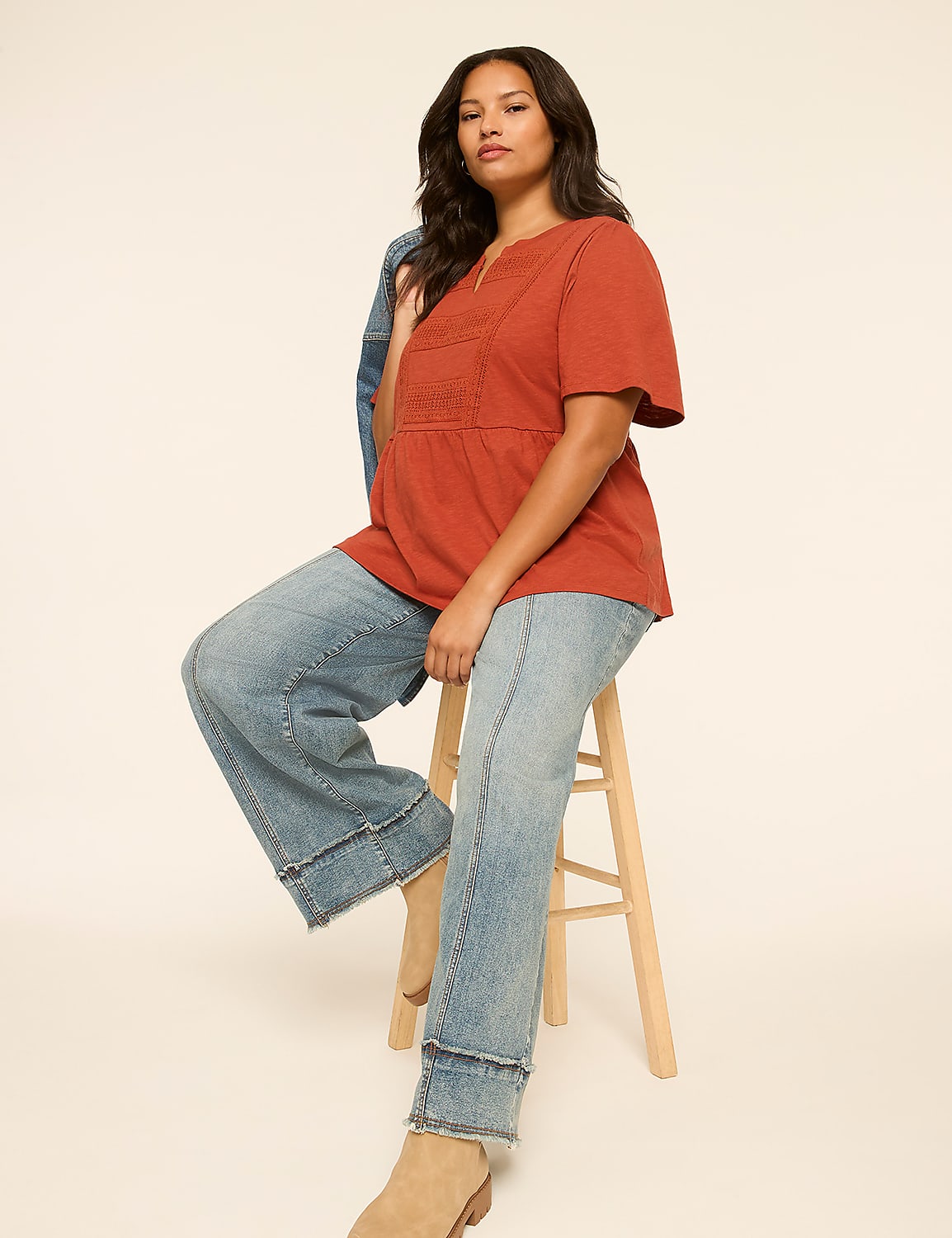 A woman in a rust-colored top and wide-leg jeans sits on a stool against a plain, light-colored background. Product Image 3