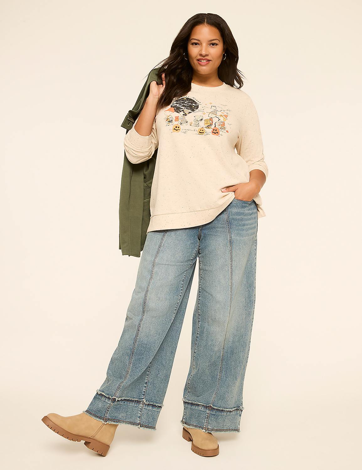 A woman in a cream-colored sweatshirt and wide-leg jeans poses against a plain, light-colored background, with a green jacket draped over her shoulder. Product Image 3