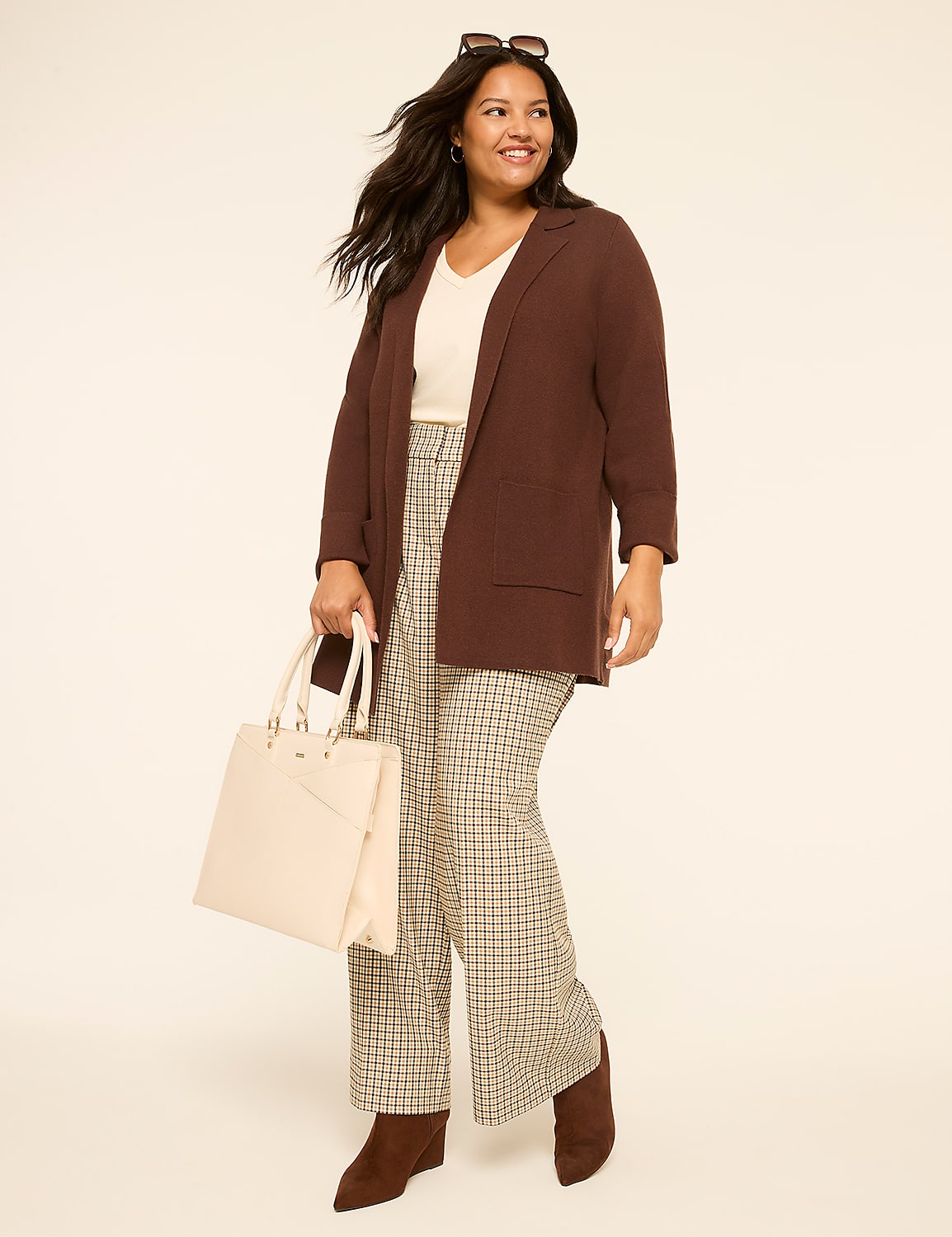 A smiling woman in a brown cardigan and plaid pants holds a cream tote bag against a plain, light-colored background. Product Image 3