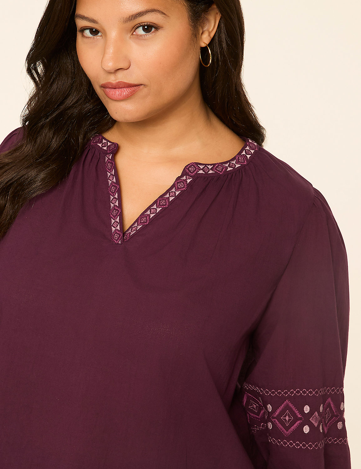 A woman in a plum-colored blouse with embroidered details on the neckline and sleeves poses against a plain beige background. Product Image 4