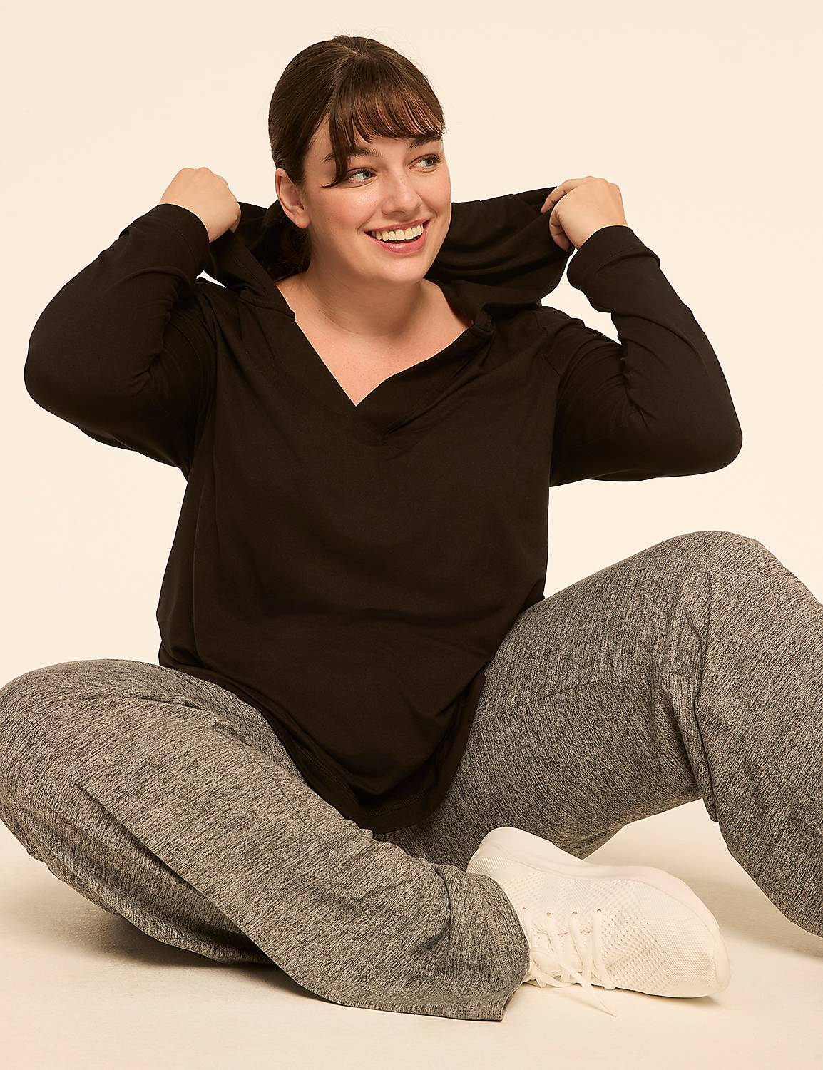 A smiling woman in a black hoodie and gray sweatpants sits on a plain, light-colored background. Product Image 3