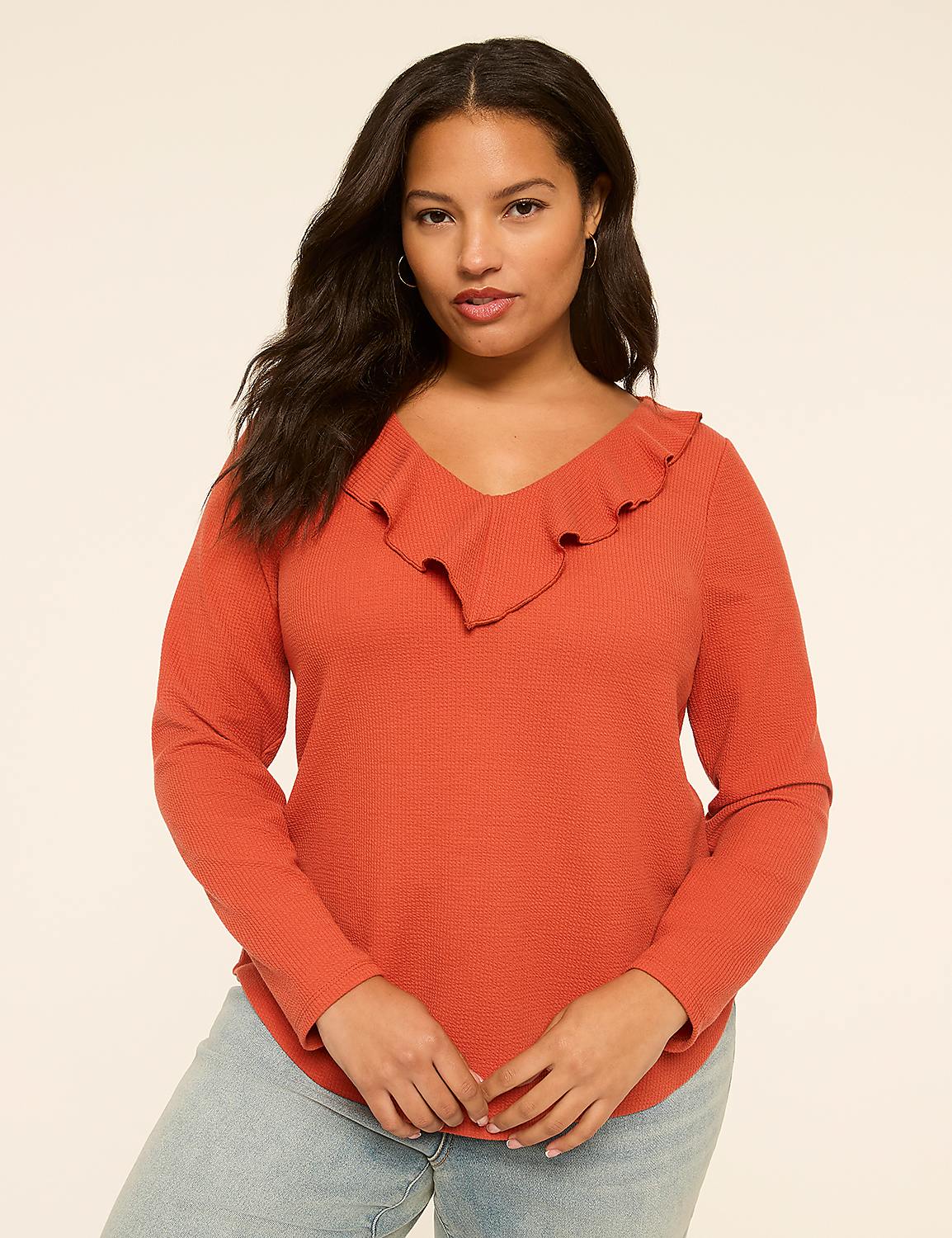 A woman with dark wavy hair and a rust-colored ruffled V-neck shirt stands against a plain, light-colored background. Product Image 1