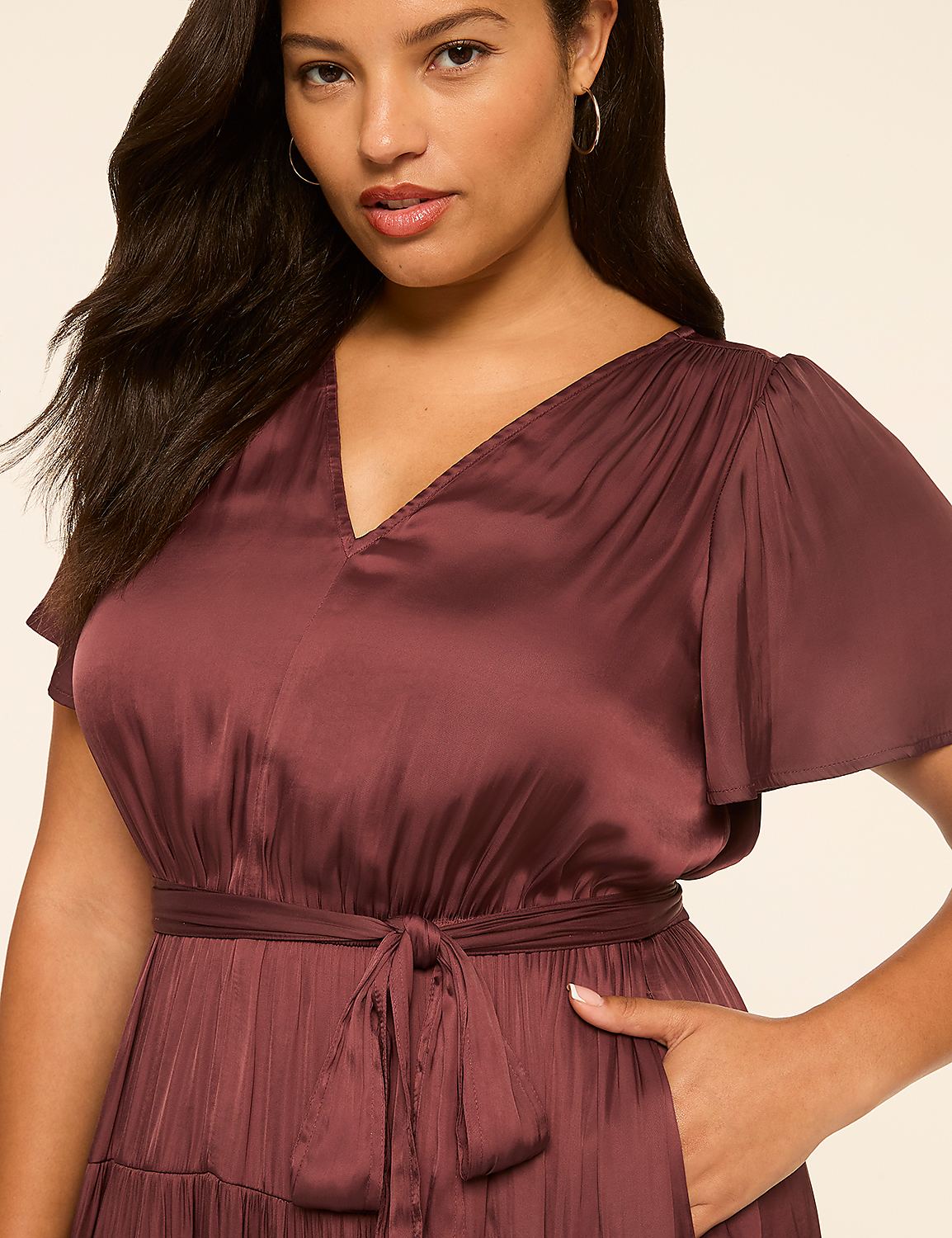 A woman in a burgundy satin dress with flutter sleeves and a tie waist stands against a plain, light-colored background. Product Image 3