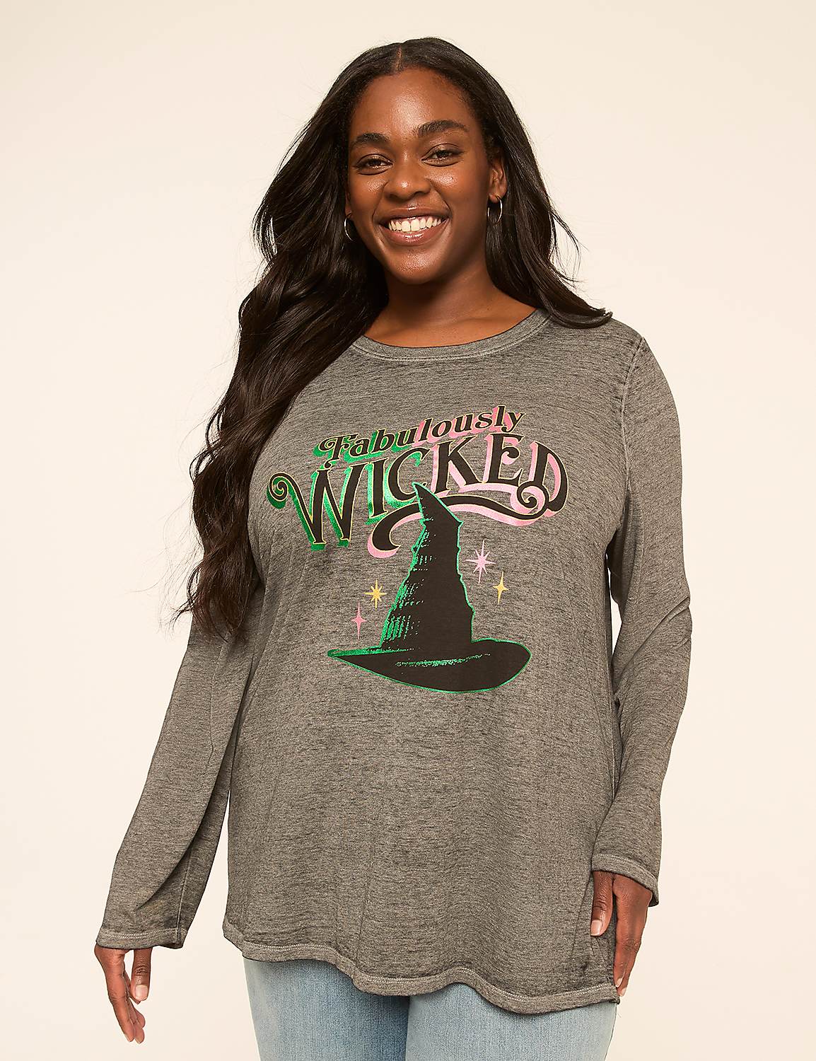 A smiling woman in a long-sleeved shirt with a witch hat graphic stands against a plain, light-colored background. Product Image 1