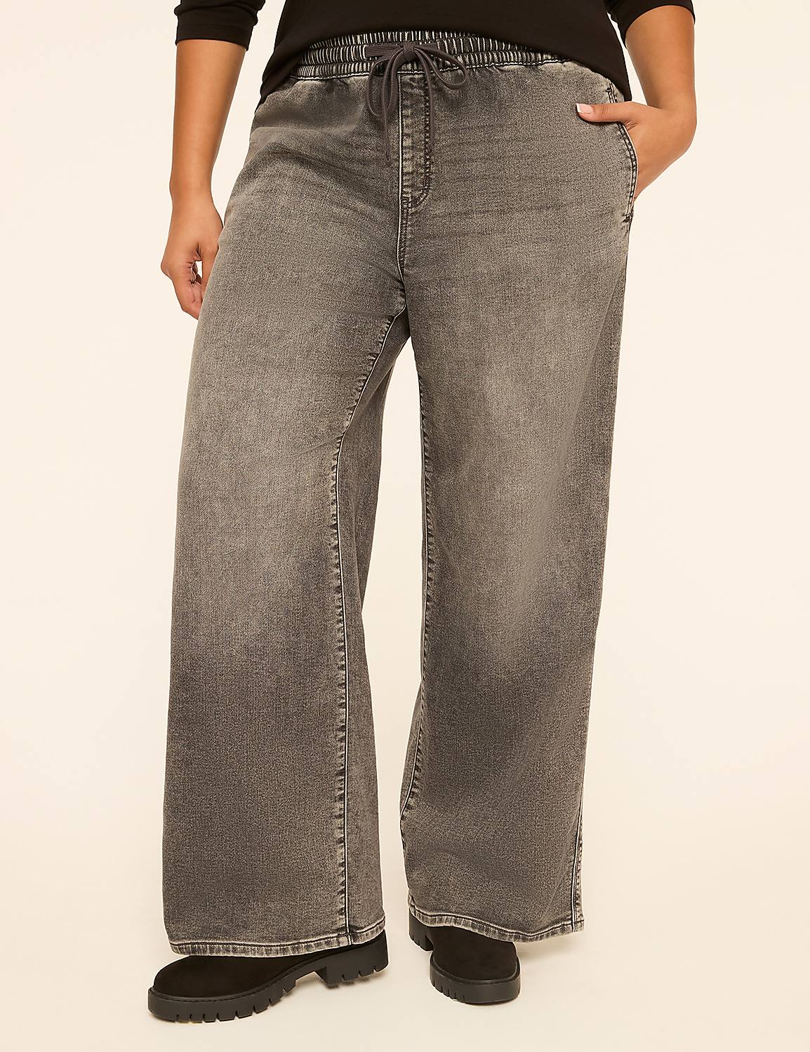 A person stands in wide-leg grey denim pants with a drawstring waist and black boots, against a plain cream background. Product Image 1