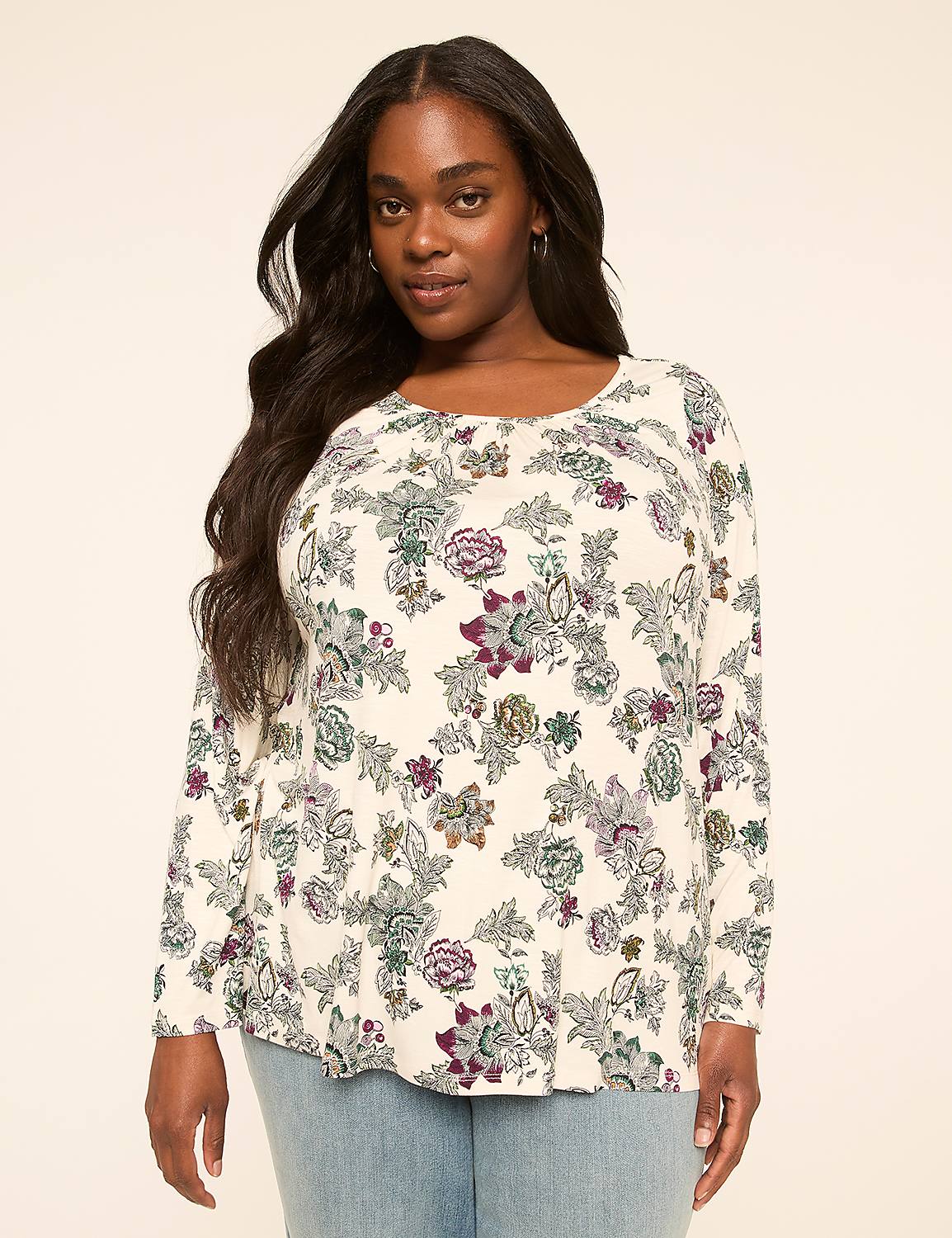 A woman with long, dark hair stands in the foreground wearing a cream-colored, long-sleeved shirt with a floral pattern, against a plain, light-colored background. Product Image 1