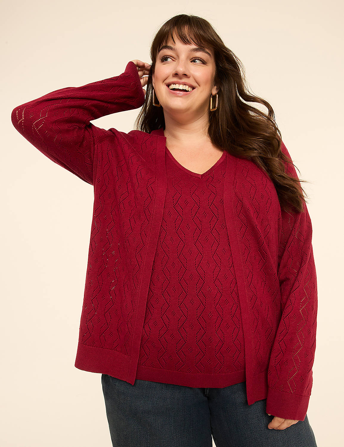 A smiling woman in a red knit sweater and blue jeans poses against a plain cream background. Product Image 1