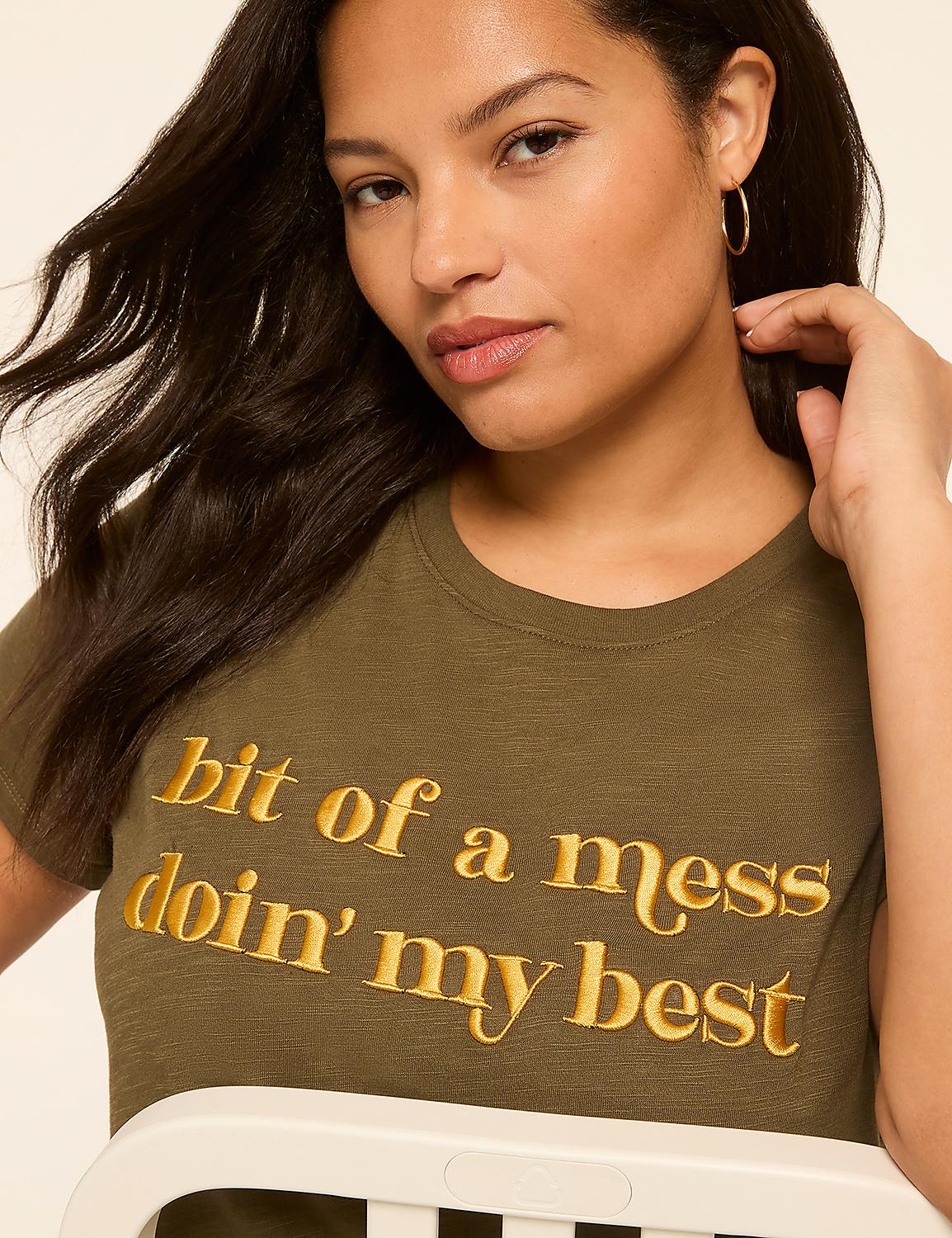 A woman with dark hair and hoop earrings wears a green t-shirt with gold lettering that reads "bit of a mess doin' my best," against a plain, light-colored background. Product Image 4