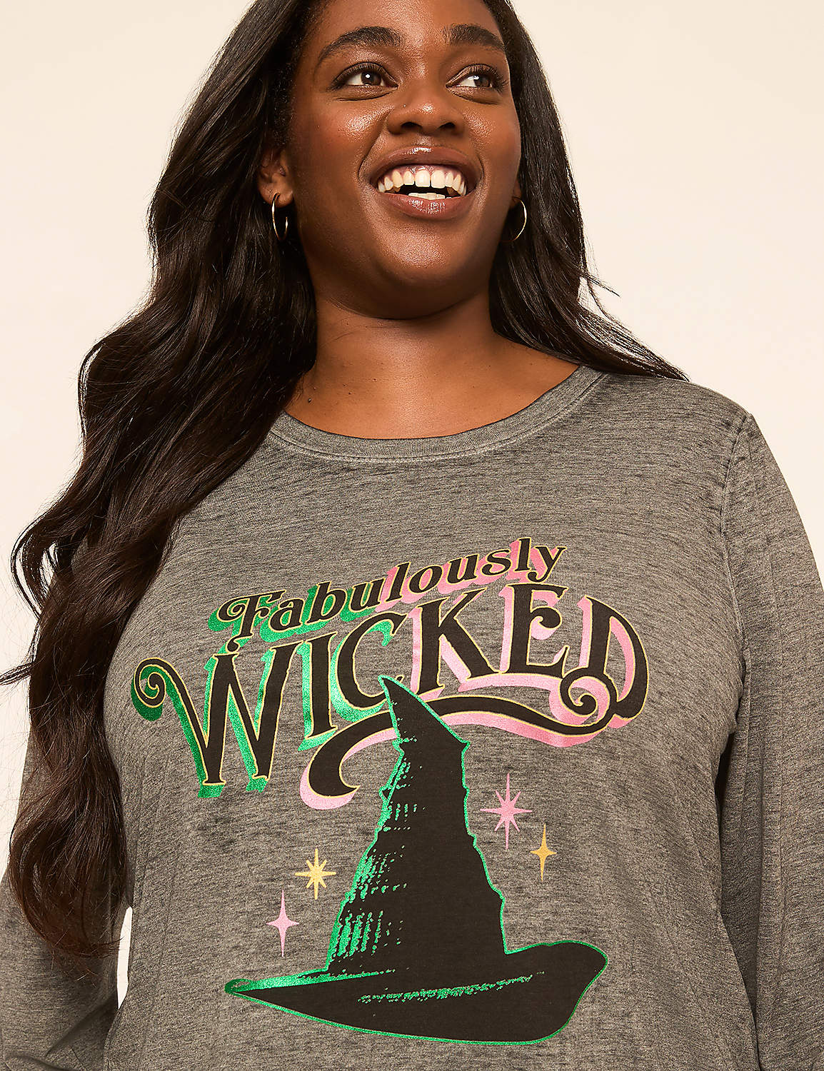 A smiling woman in a gray long-sleeved shirt with a "Fabulously Wicked" graphic and a witch's hat is shown against a plain, light-colored background. Product Image 4