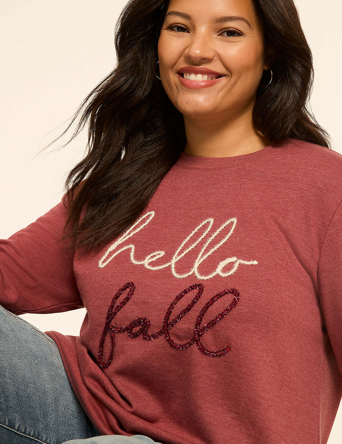 A smiling woman in a maroon sweatshirt with "hello fall" embroidered on it poses against a plain, light-colored background. Product Image 4