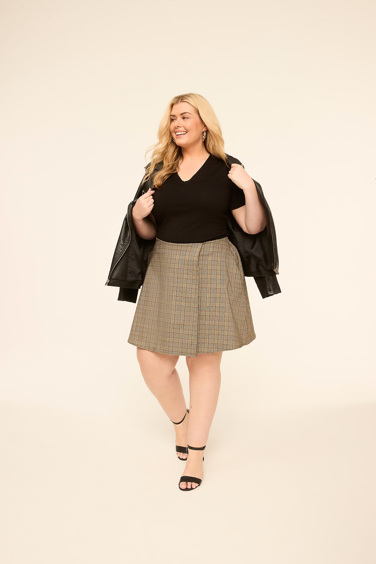 A smiling woman in a black top, patterned skirt, and leather jacket stands against a plain, light-colored background. Product Image 4