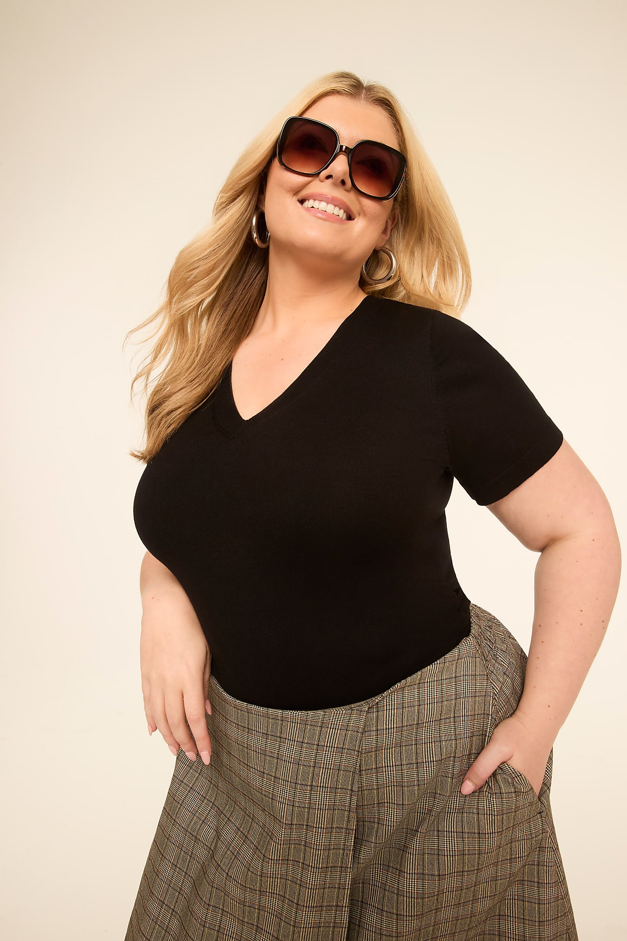 A smiling woman with blonde hair and large sunglasses poses in the foreground against a plain, light-colored background. Product Image 7